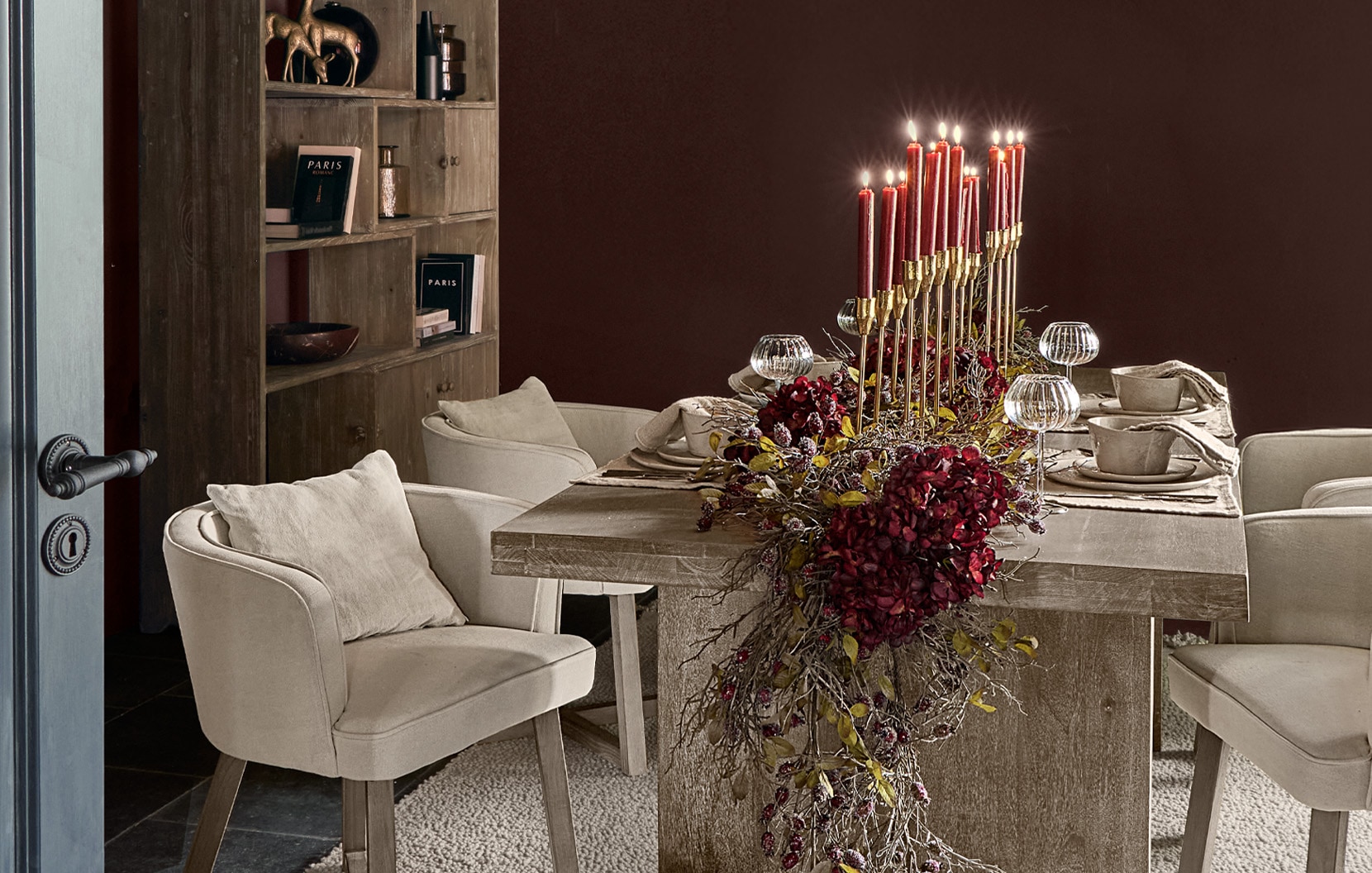 Salle à manger avec table en bois, fauteuils crème et décoration centrale de bougies rouges et fleurs