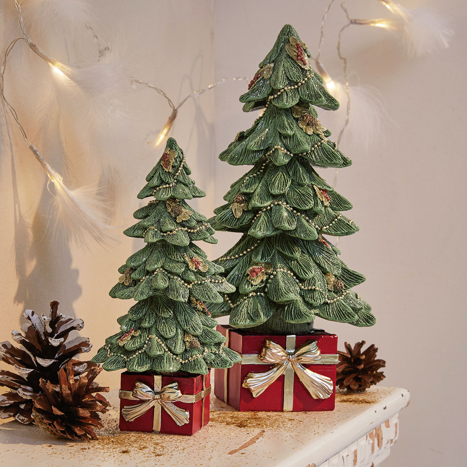 Lot de 2 sapins décoratifs Verne Deux sapins décoratifs verts en matériau sur des boîtes rouges avec nœuds dorés, décoration de Noël sur table