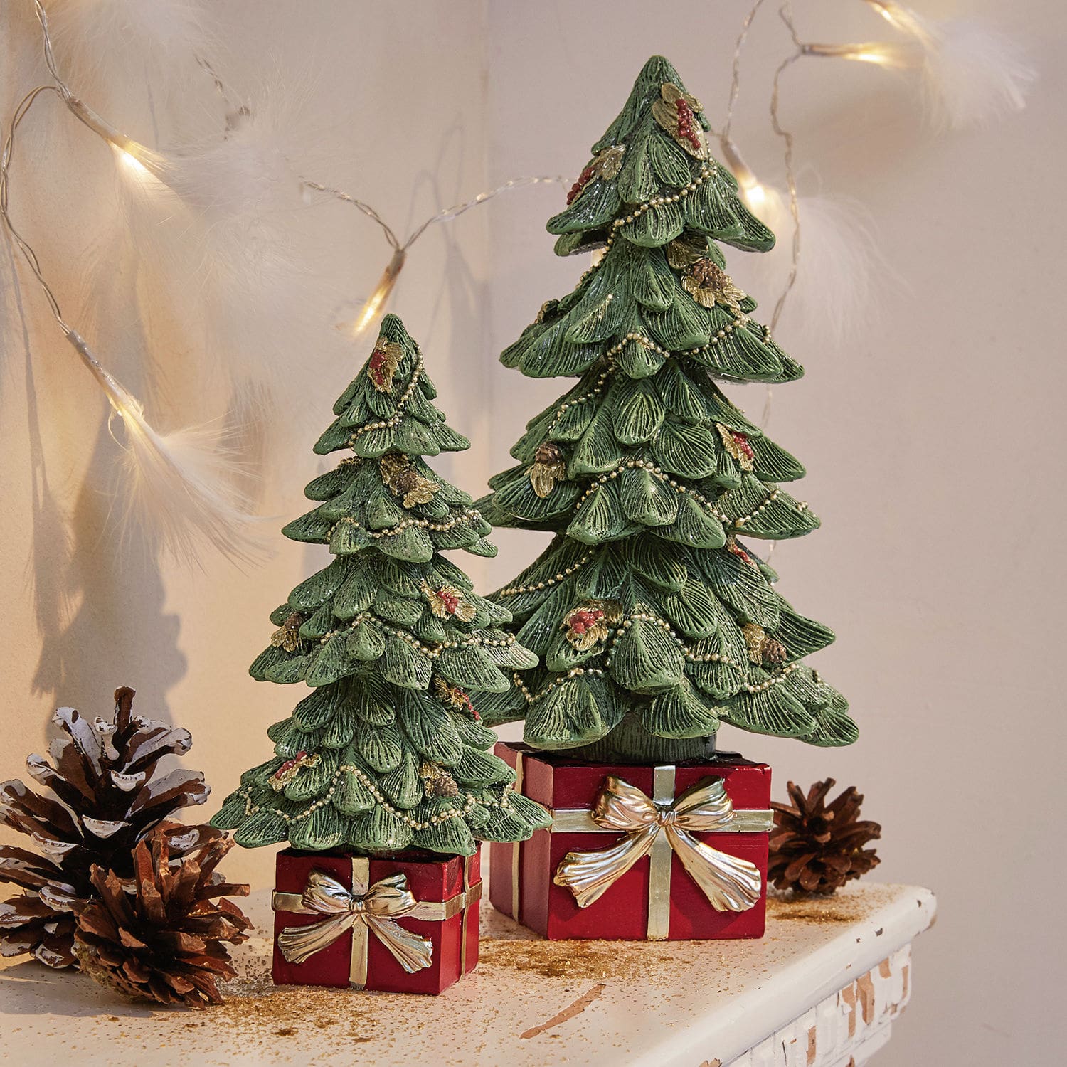 Lot de 2 sapins décoratifs Verne Deux sapins décoratifs verts en matériau sur des boîtes rouges avec nœuds dorés, décoration de Noël sur table