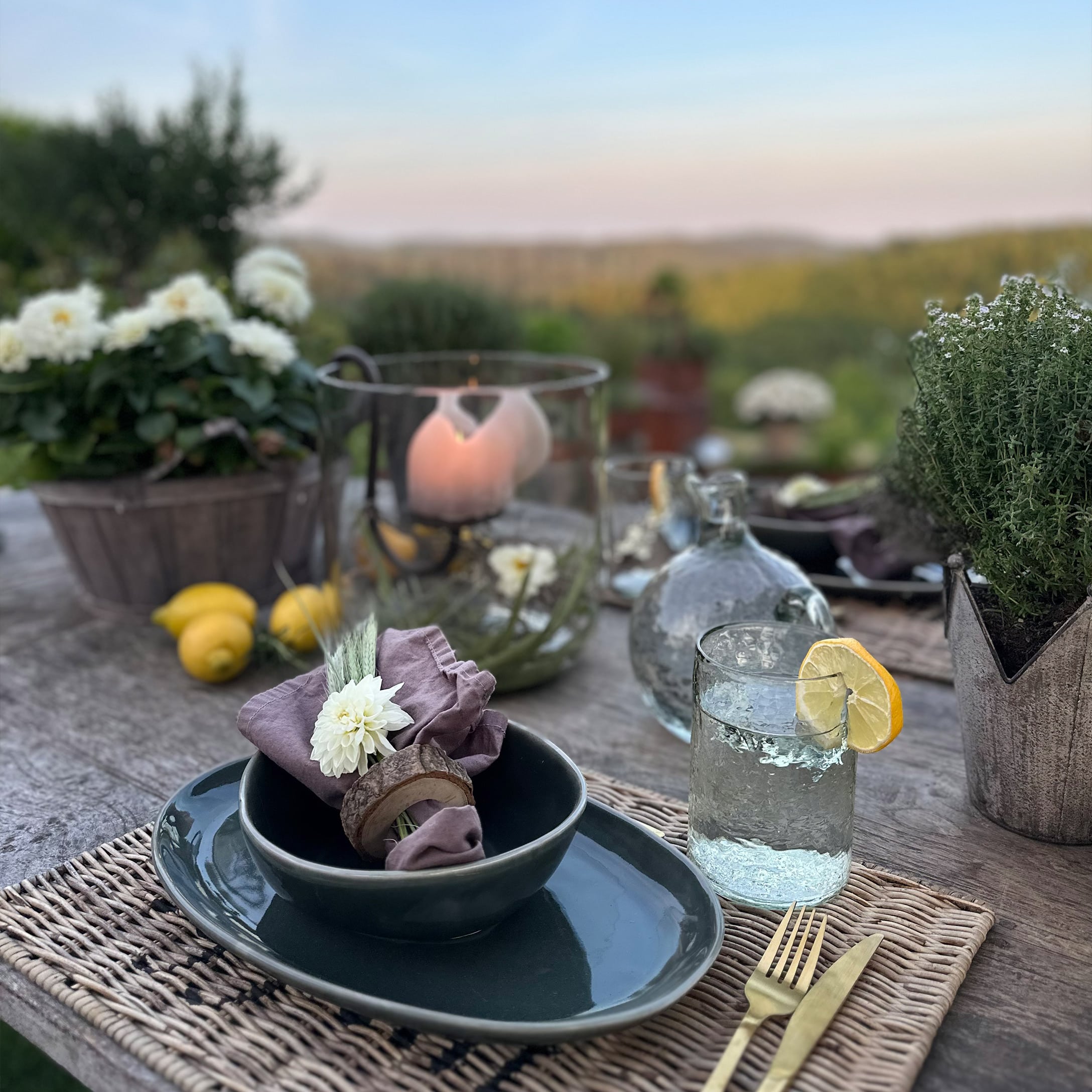 Table rustique avec vaisselle en céramique sombre, serviette en lin et verre d'eau citronnée en extérieur