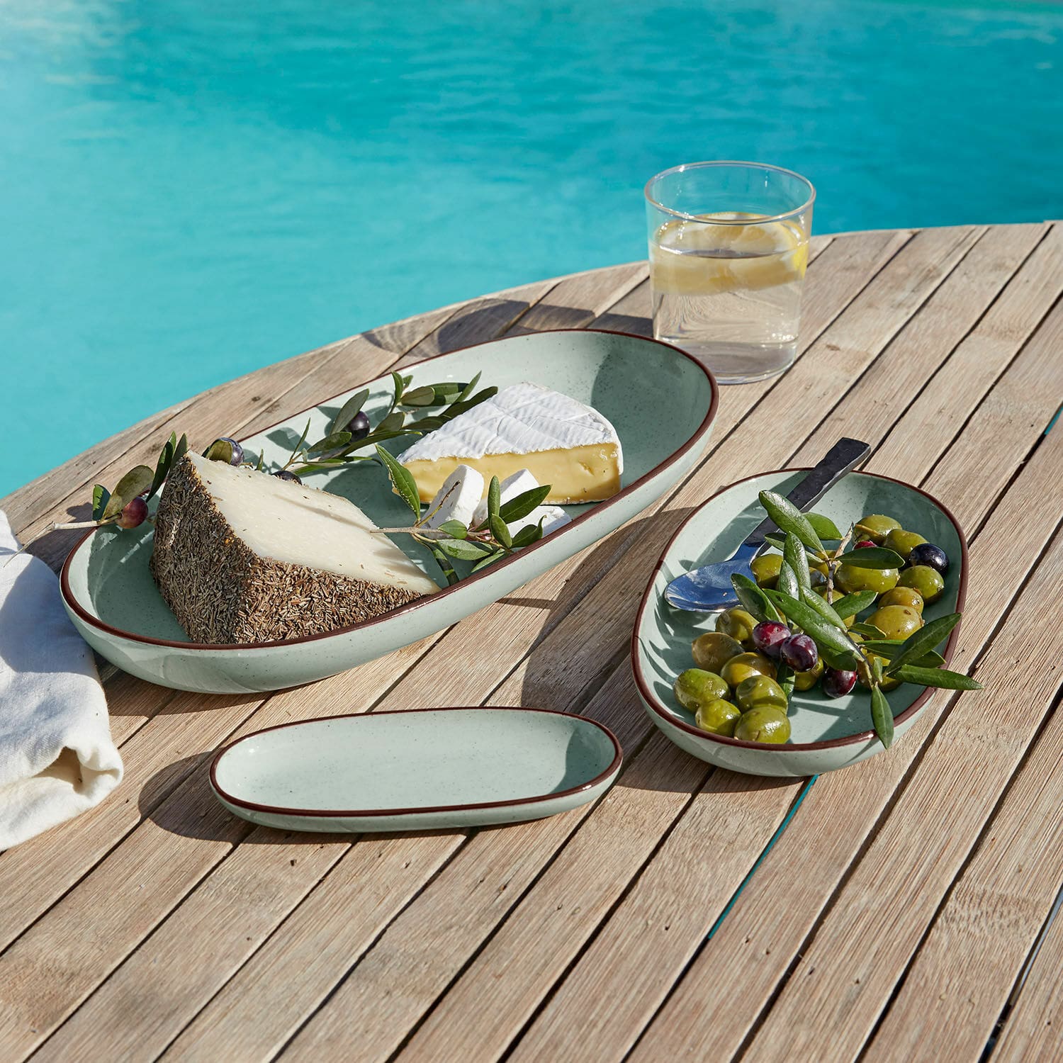 Lot de 3 plateaux de service Biarré Ensemble de trois assiettes ovales en céramique vert clair avec bord brun sur table en bois près de la piscine