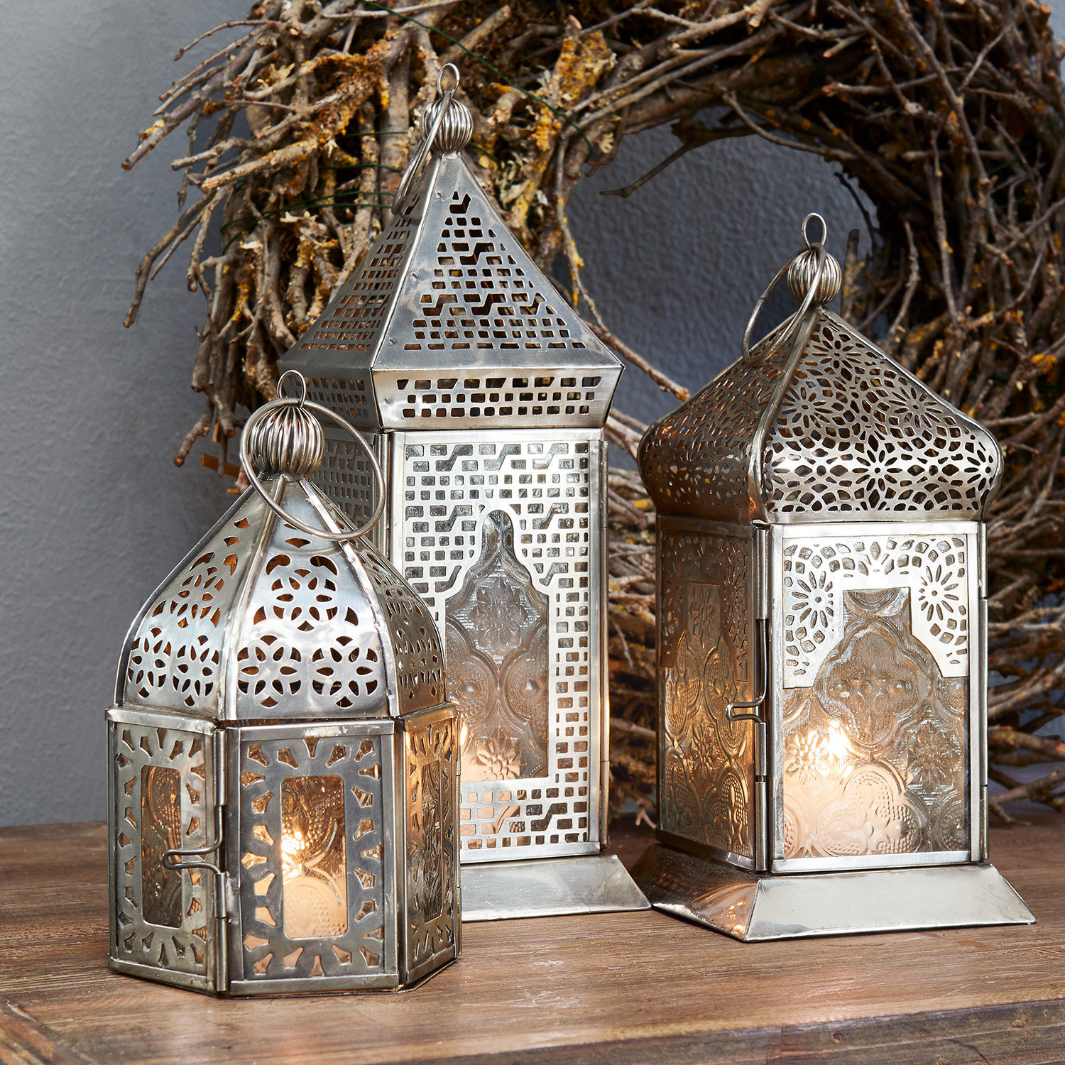 Lot de 3 lanternes Indian Trois lanternes en métal argenté avec motifs ajourés et panneaux en verre sur une table en bois
