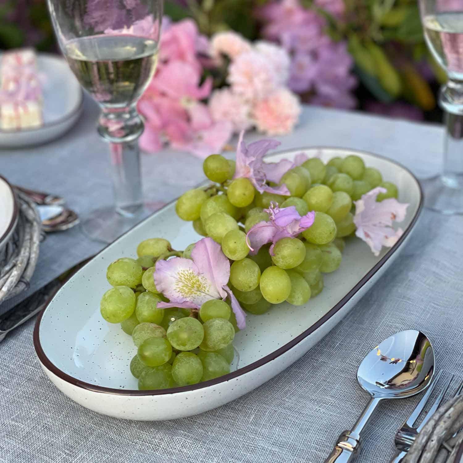 Raisins verts avec fleurs roses sur une assiette en céramique blanche posée sur une nappe grise