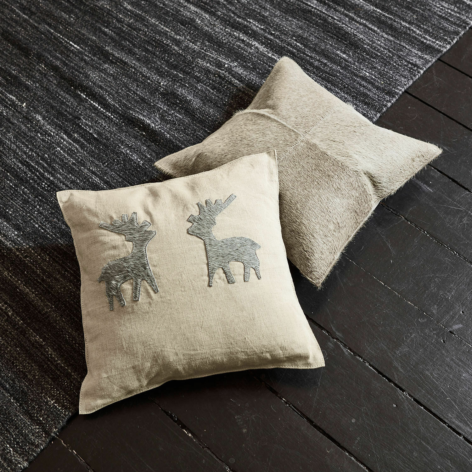 Lot de 2 housses de coussins Beaupuy Coussin beige en lin avec motifs cerfs gris et coussin en cuir clair sur sol foncé et tapis gris