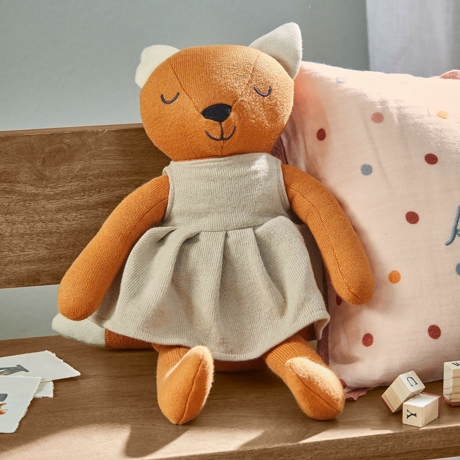 Peluche Fuzzlin Peluche renard orange en robe beige assise sur un banc en bois avec coussin et cubes en bois