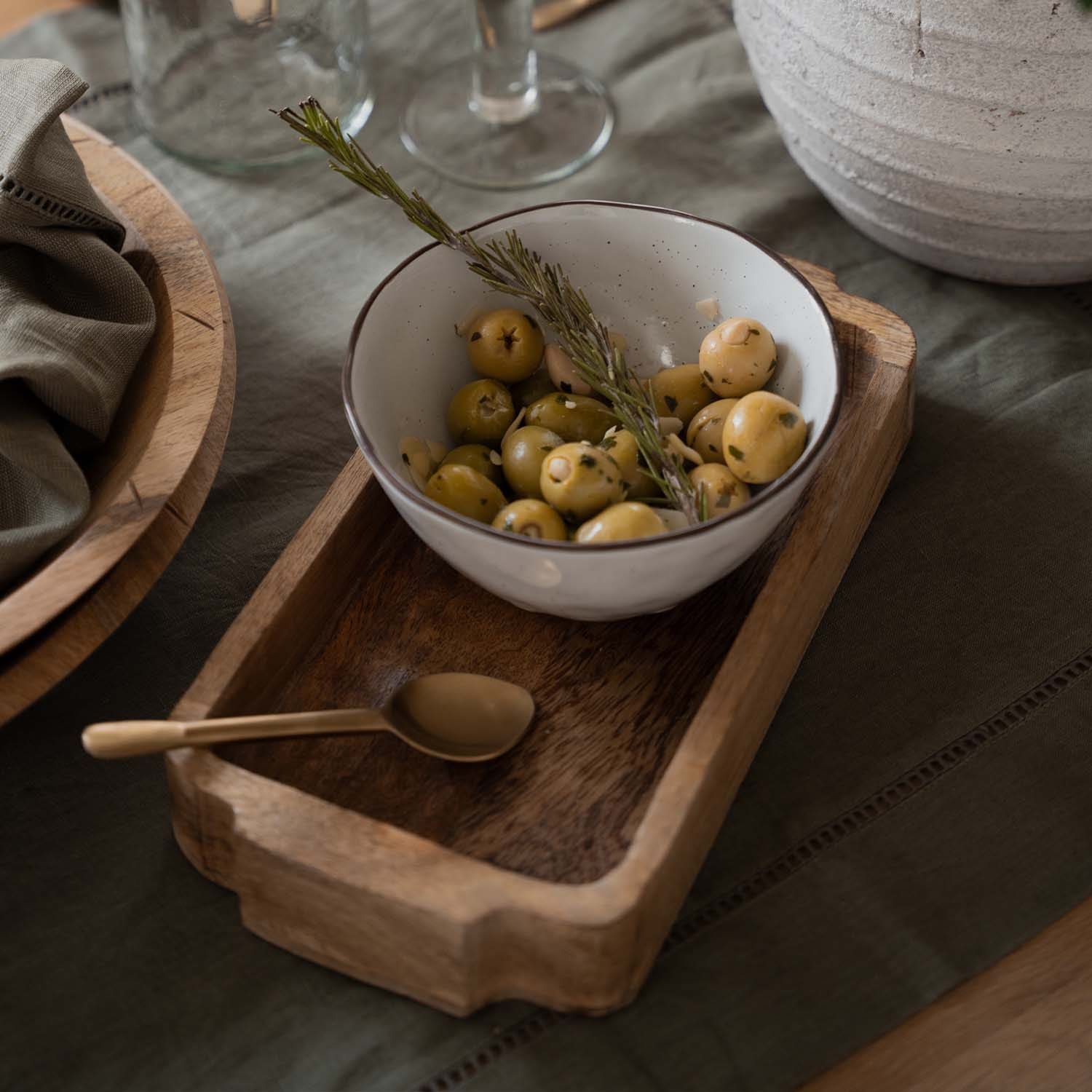 Bol en céramique blanche avec olives vertes et branche de romarin sur plateau en bois