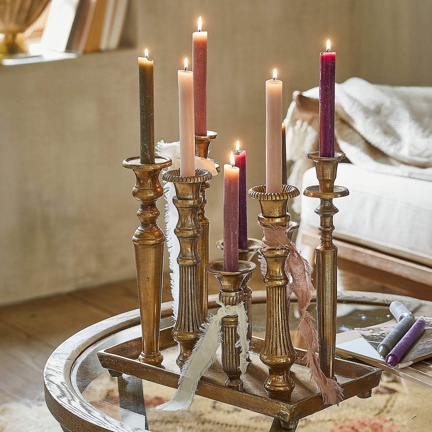 Plateau à bougies Chavelot Ensemble de chandeliers en métal doré avec bougies colorées allumées sur une table en verre