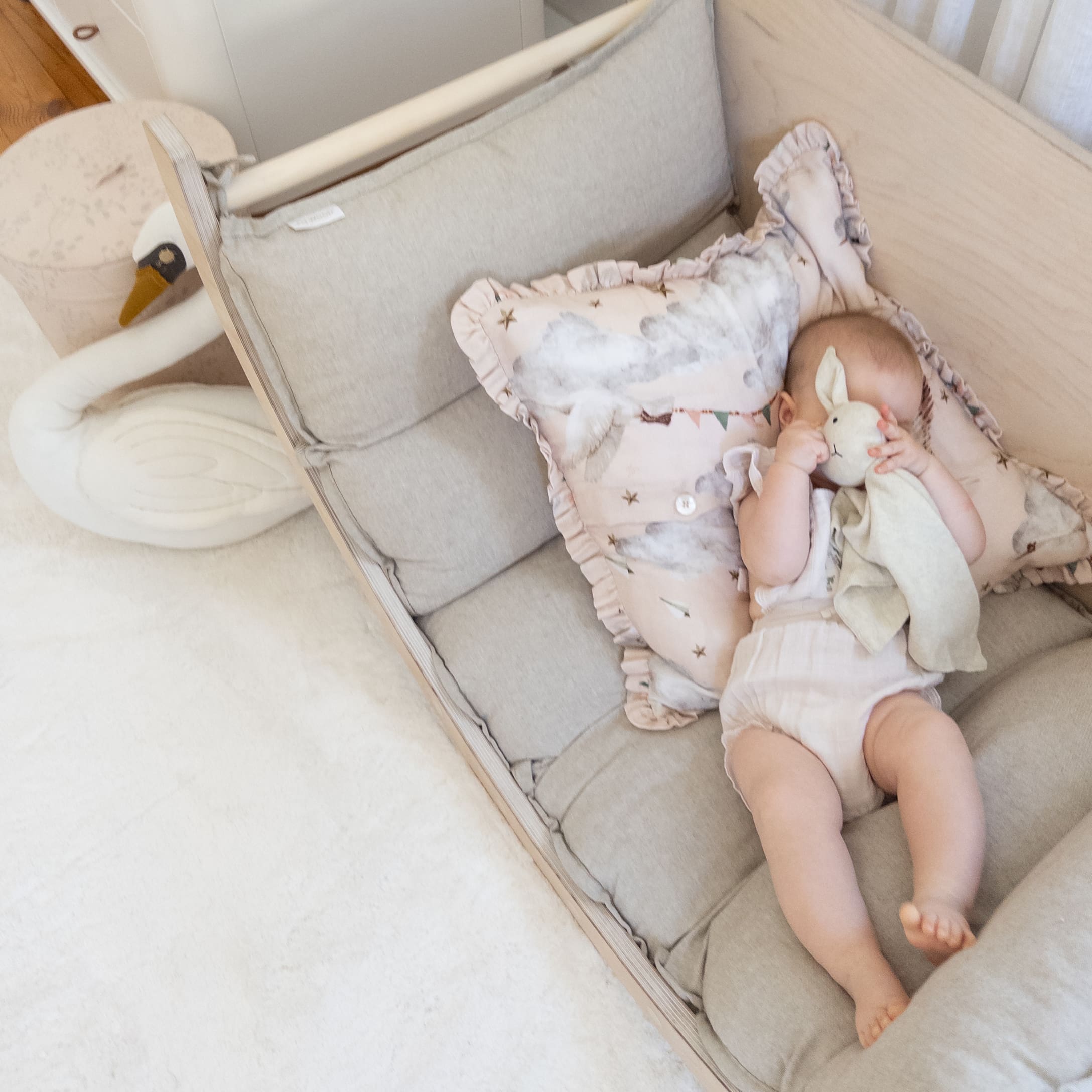 Bébé allongé sur un matelas gris avec un coussin nuage et un doudou lapin dans une chambre d'enfant claire
