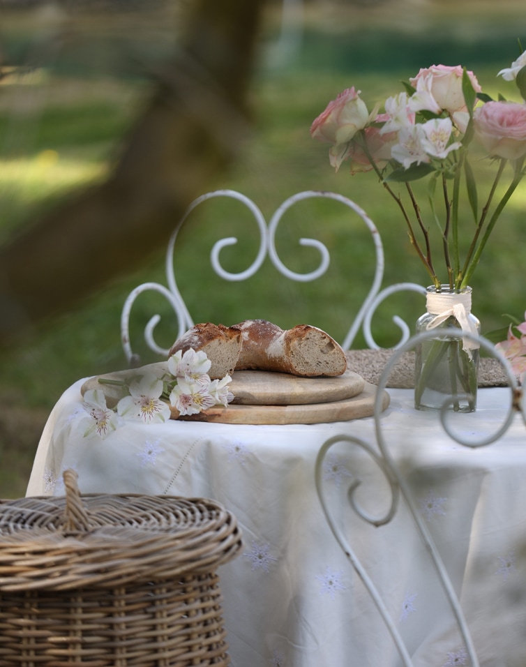 Pain rustique sur planche en bois sur une table avec nappe blanche et bouquet de fleurs roses dans un jardin