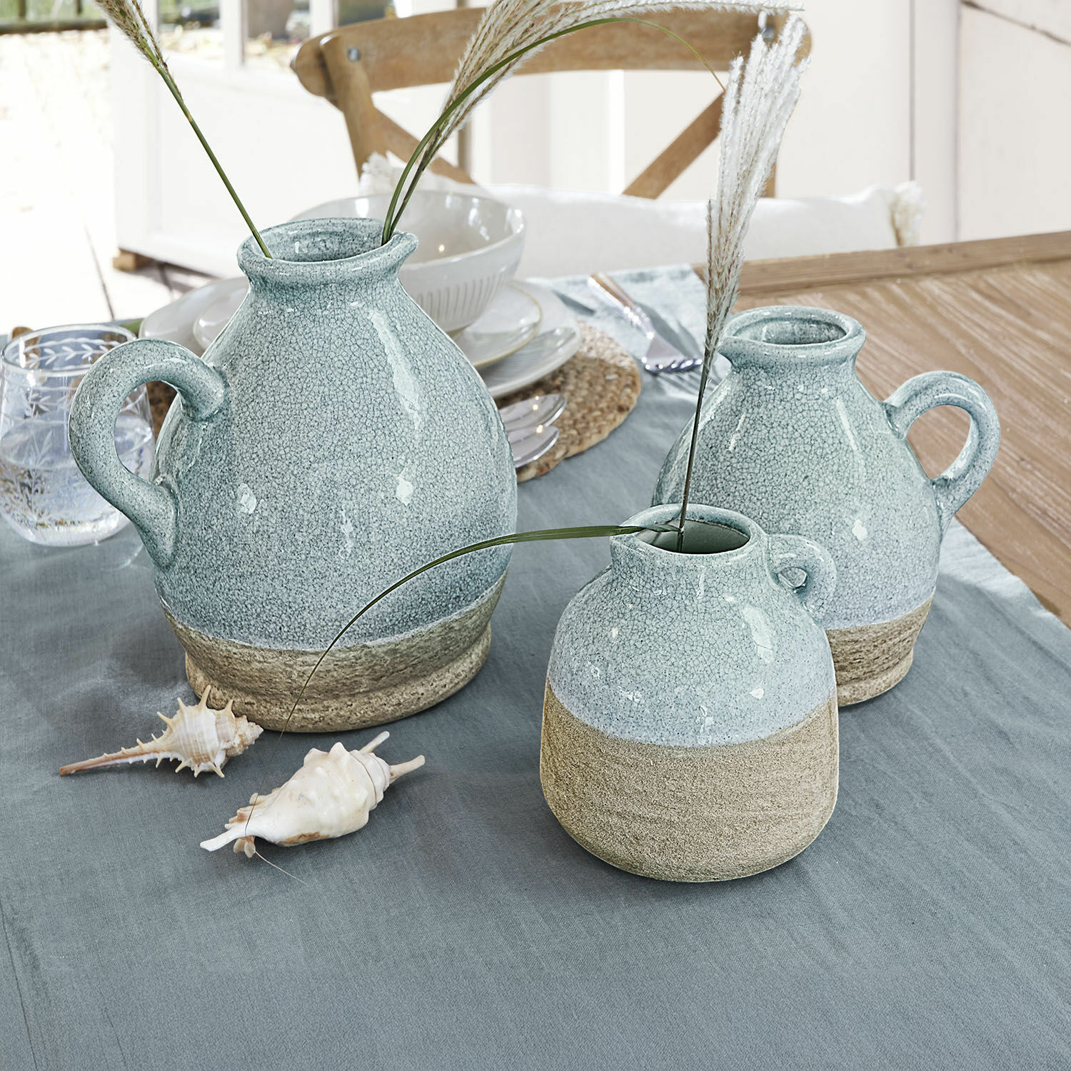 Lot de 3 vases Lezíria Ensemble de trois vases en céramique bleu clair et beige posés sur une table avec des coquillages