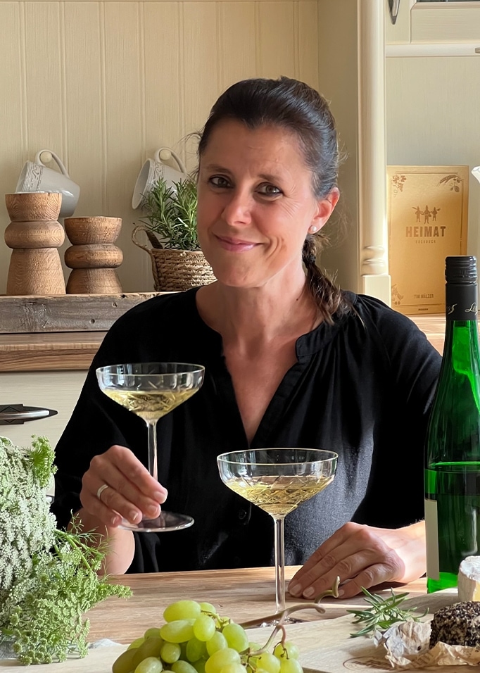Femme en chemise noire tenant un verre de vin blanc à table avec raisins et fromages