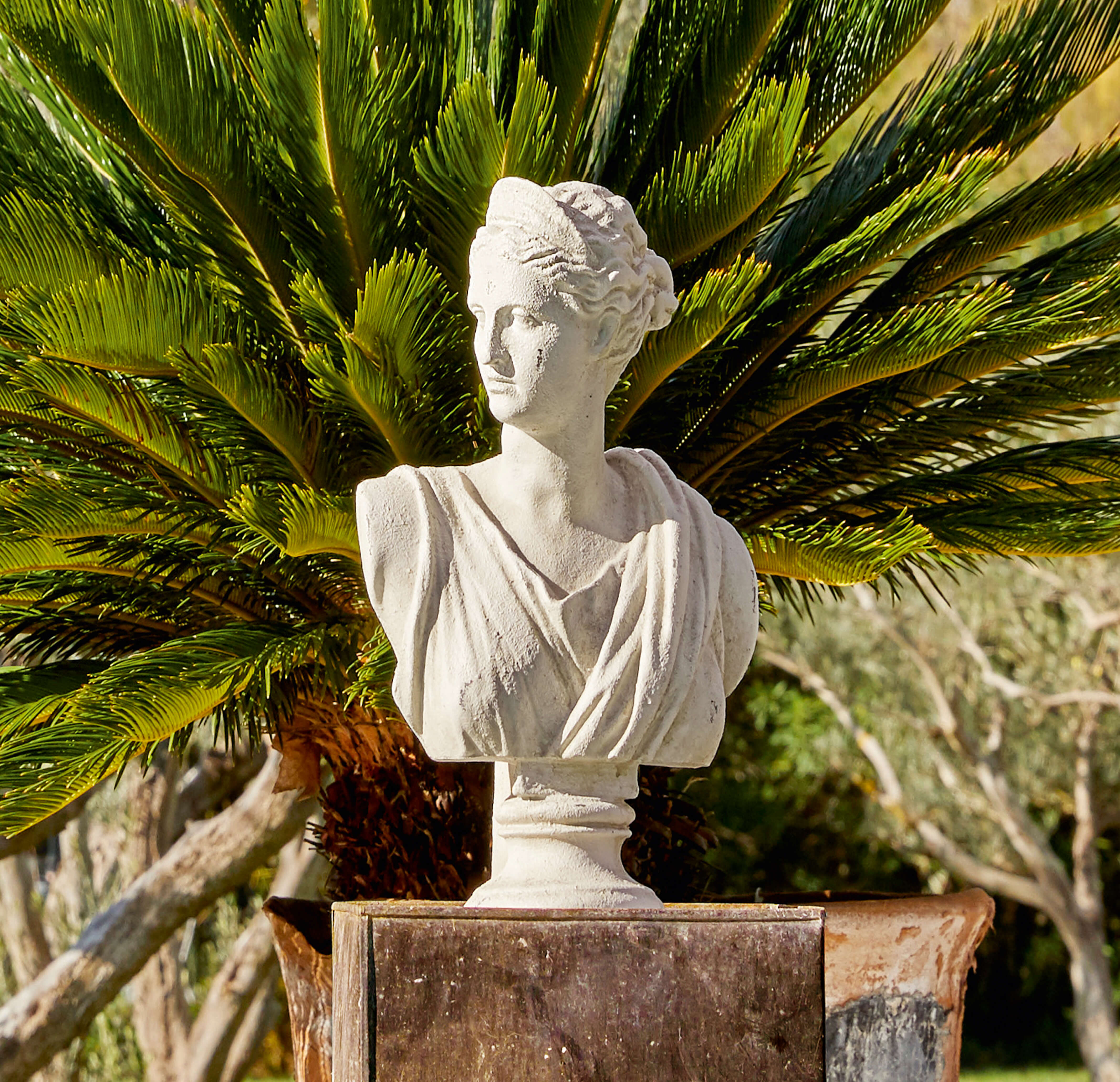 Buste blanc en pierre représentant une femme devant un palmier vert, décoration de jardin élégante