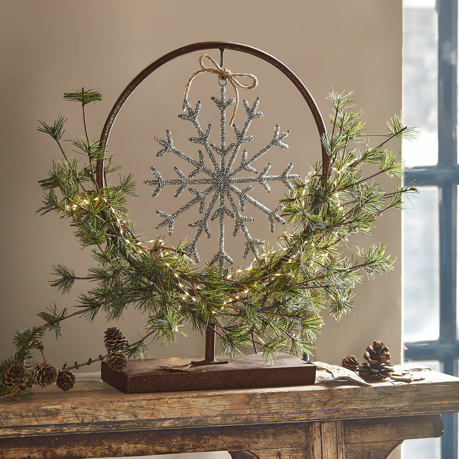 Support décoratif Nélivanne Décoration de Noël en métal avec flocon de neige argenté, branches vertes et pommes de pin sur socle en bois