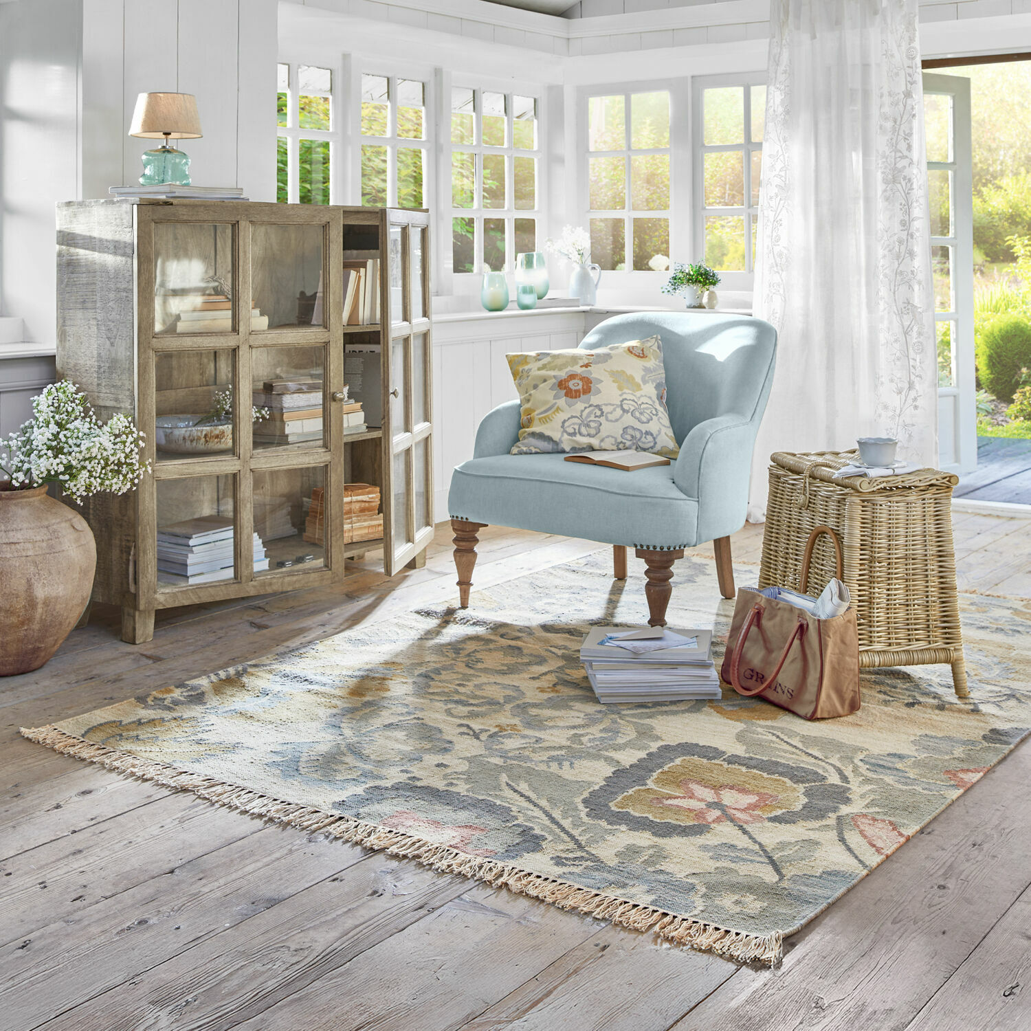 Tapis Sussex Salon lumineux avec fauteuil bleu clair, meuble en bois et tapis floral sur parquet clair
