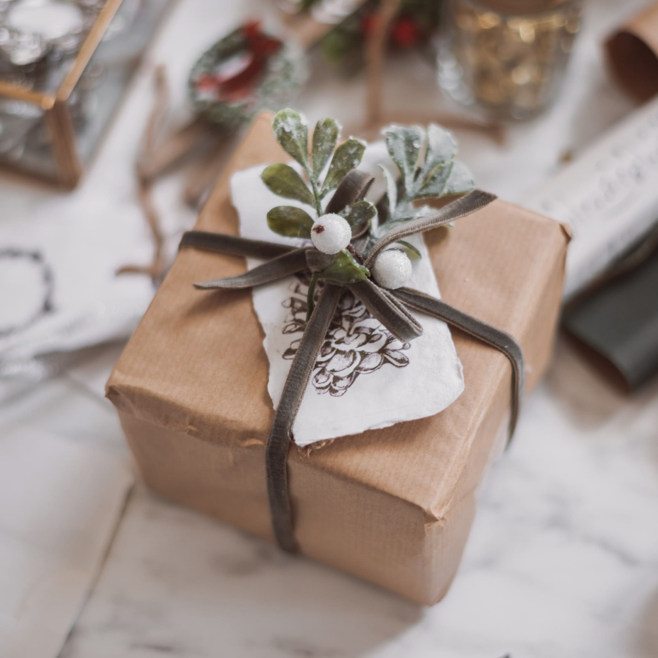 Cadeau emballé dans du papier kraft brun avec une branche décorative et des baies blanches sur un ruban