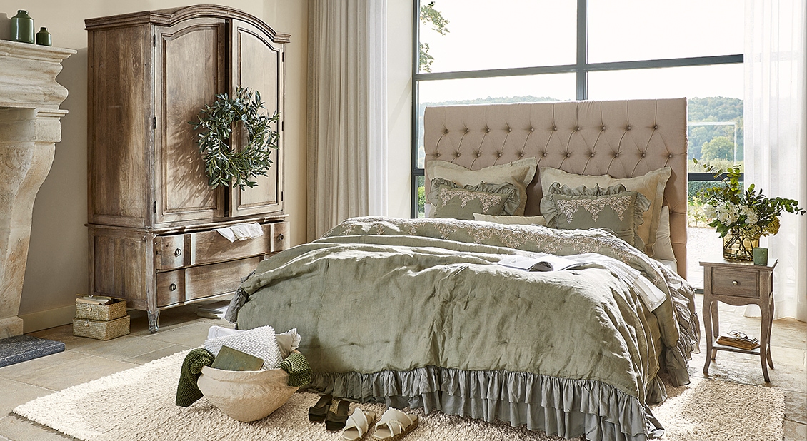 Chambre chaleureuse avec lit à tête capitonnée et linge de lit en lin vert et gris doux, ambiance naturelle