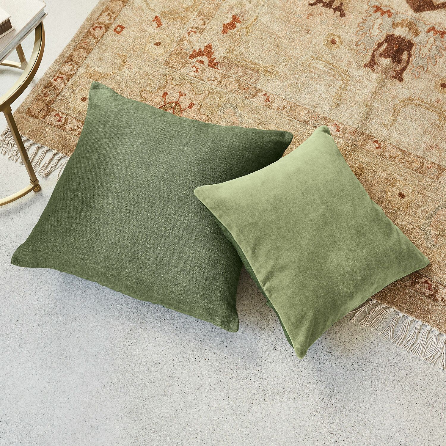 Lot de 2 housses de coussins Salina Deux coussins verts en tissus différents posés sur un tapis clair et un sol en béton