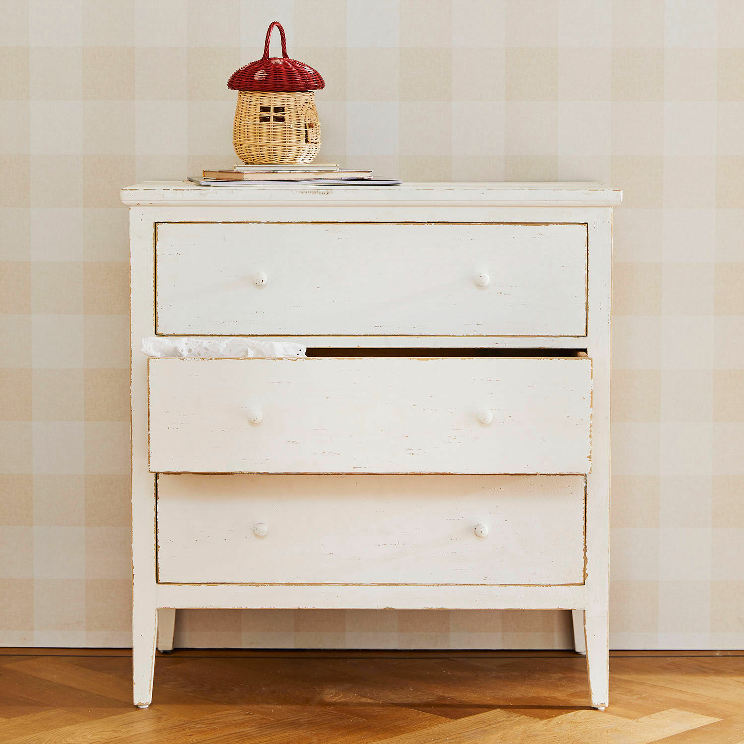 Commode Korelis Commode blanche en bois à trois tiroirs avec panier en rotin rouge et beige posé dessus