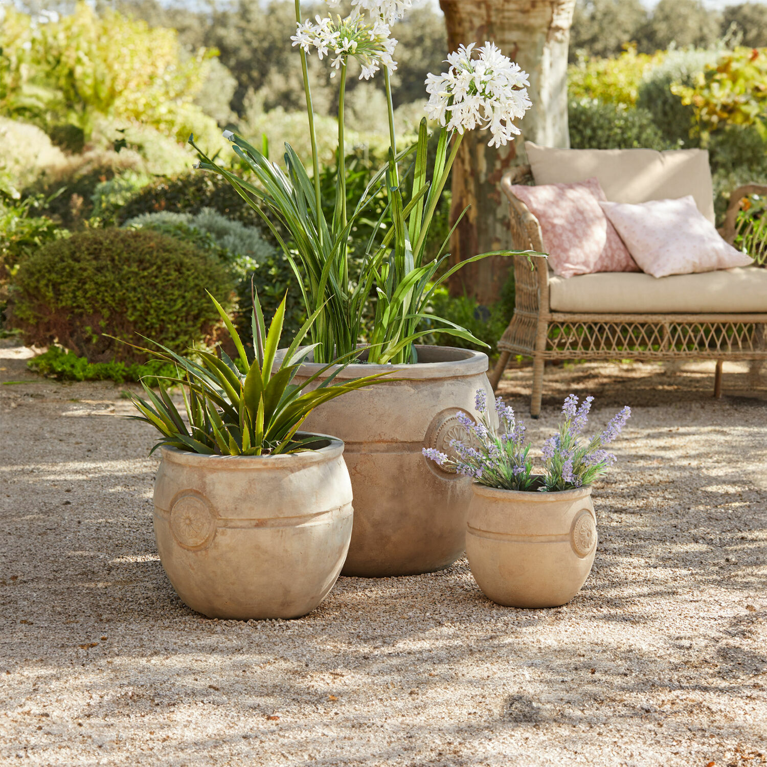 Lot de 3 pots de fleurs Clorivon Trois pots en terre cuite beige avec plantes sur patio gravillonné dans un jardin avec canapé en osier