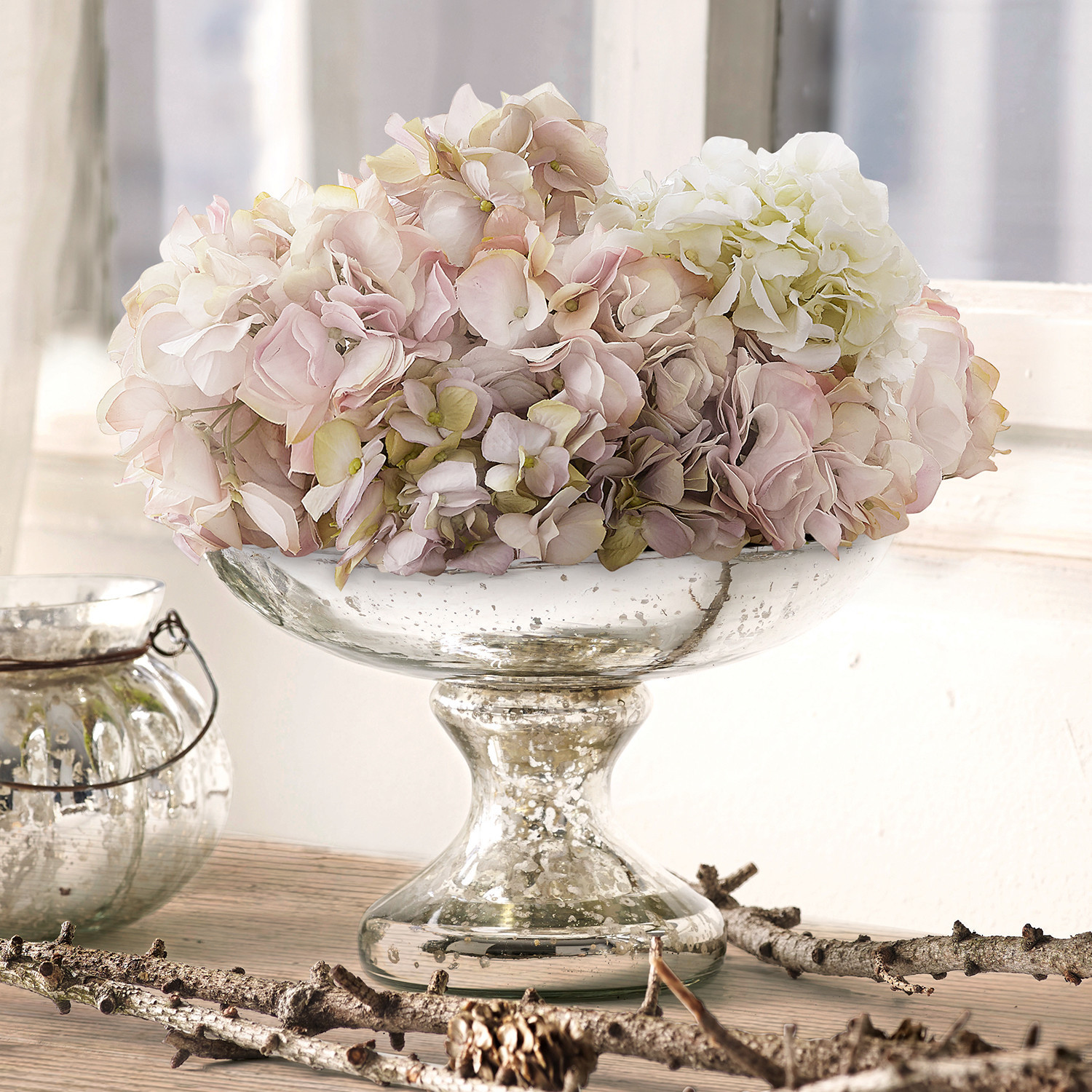 Coupe Estelle Coupe en verre sur pied avec fleurs d'hortensia pastel posée sur une table en bois clair
