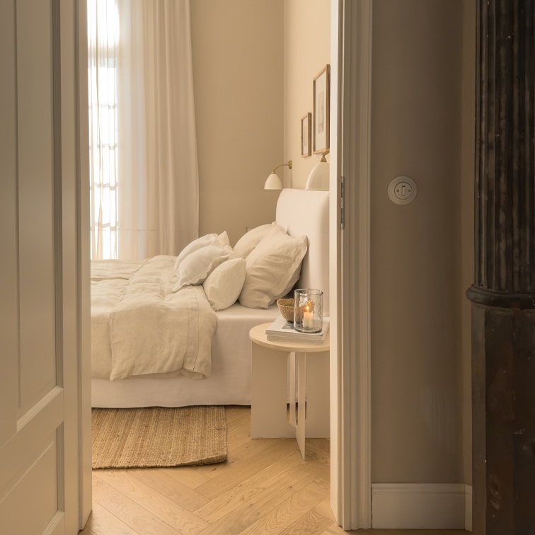 Chambre chaleureuse avec lit blanc, linge de lit beige et parquet en bois clair style scandinave