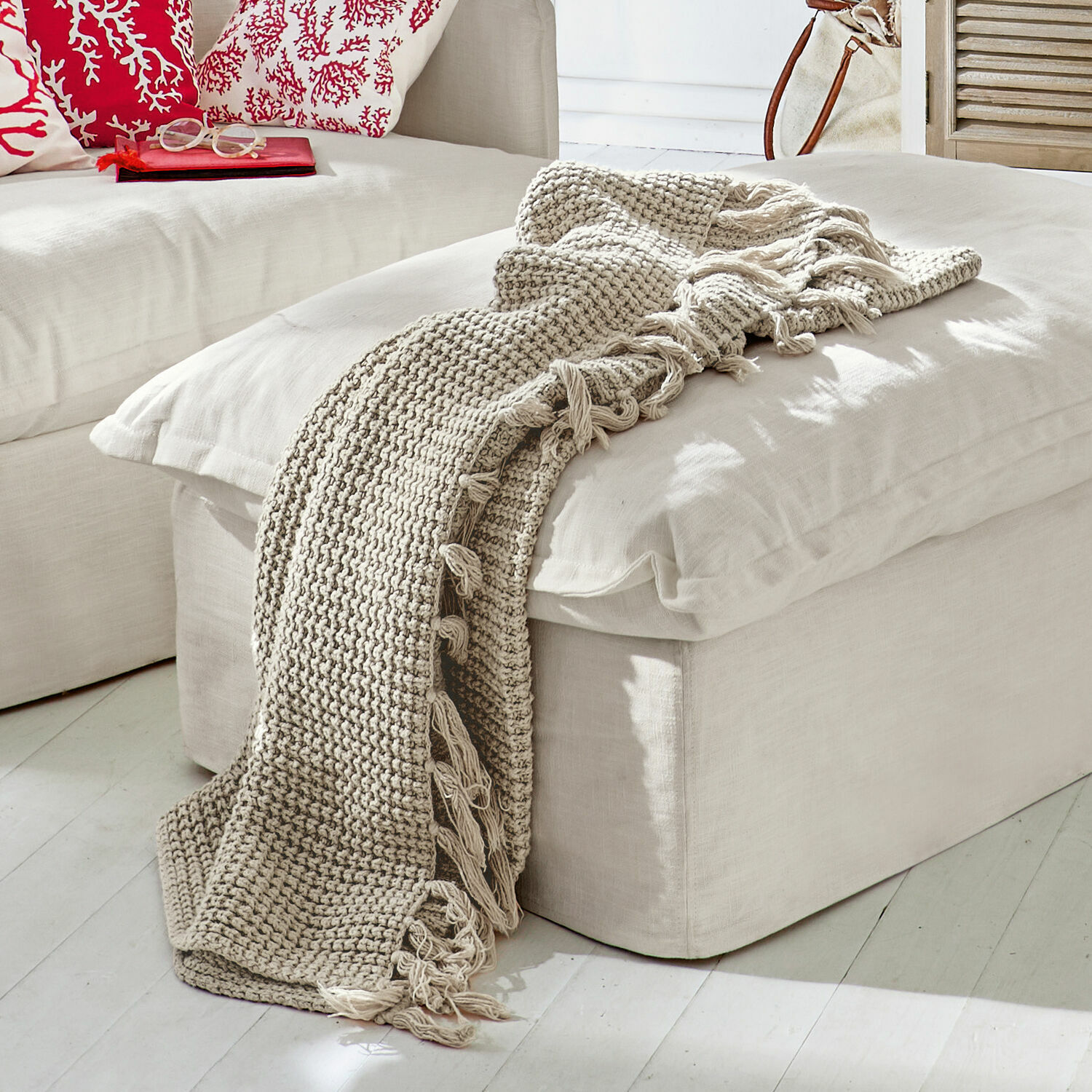 Plaid Kendall Plaid beige tricoté avec franges sur un pouf clair dans un salon lumineux