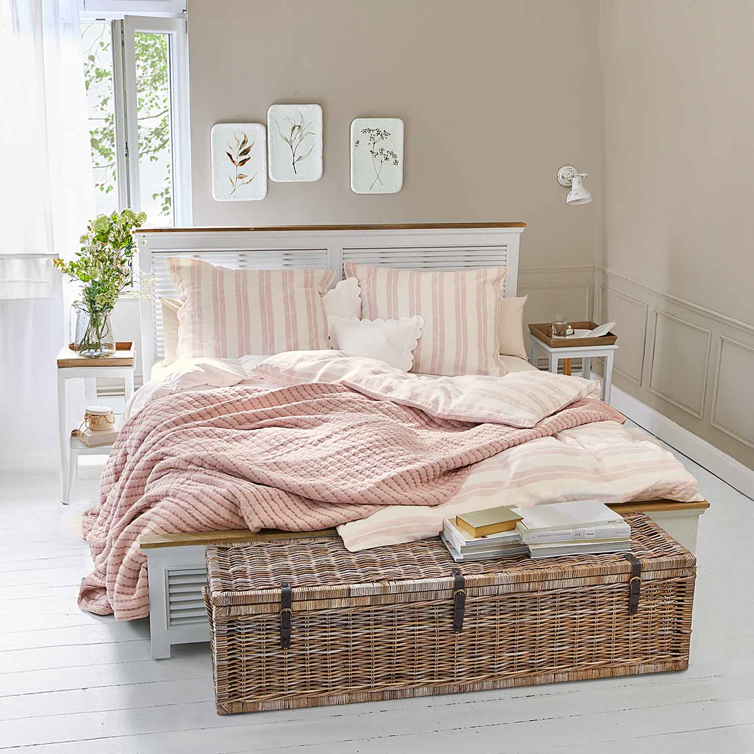 Chambre chaleureuse avec lit blanc, couverture matelassée rose et coffre en osier au sol