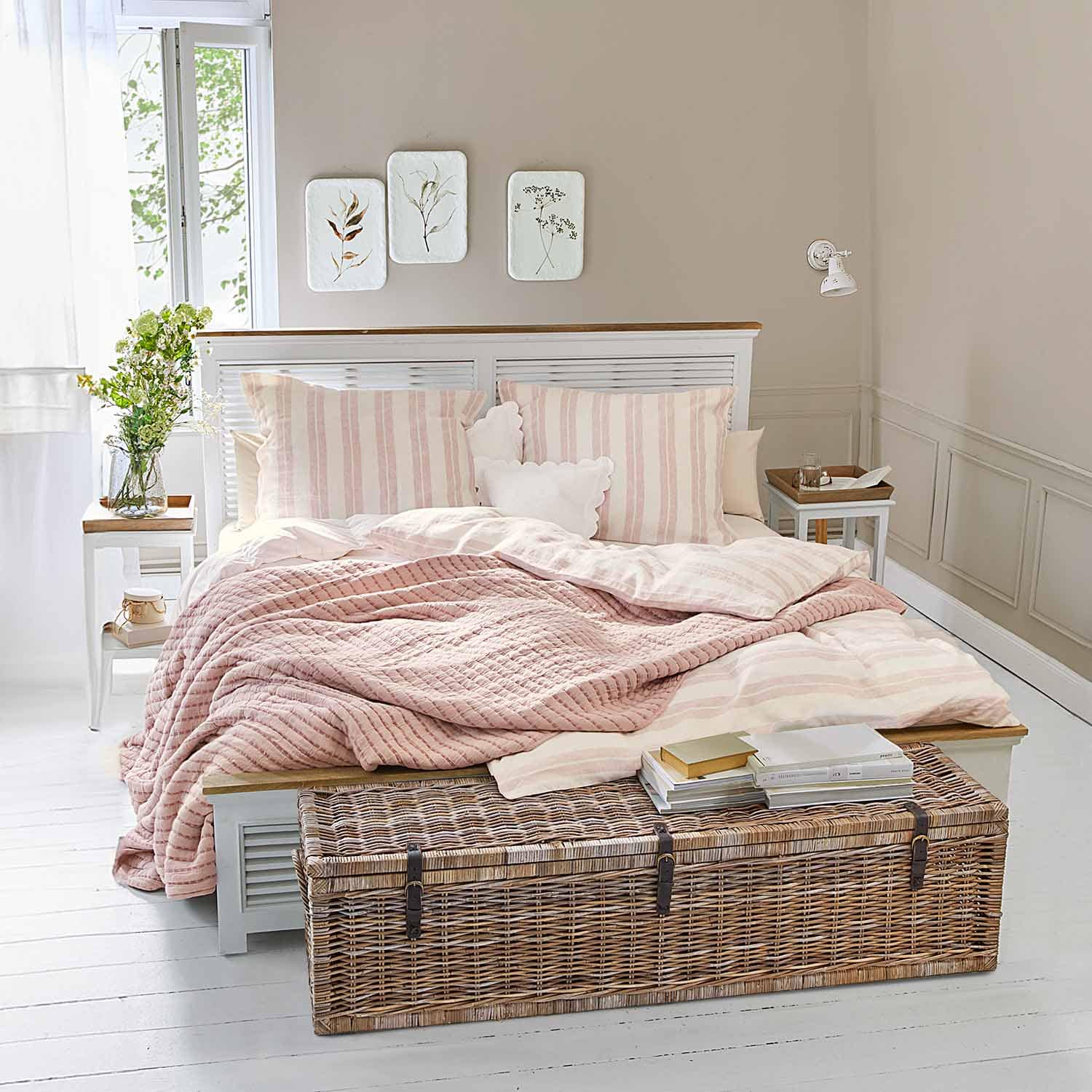 Chambre chaleureuse avec lit blanc, couverture matelassée rose et coffre en osier au sol