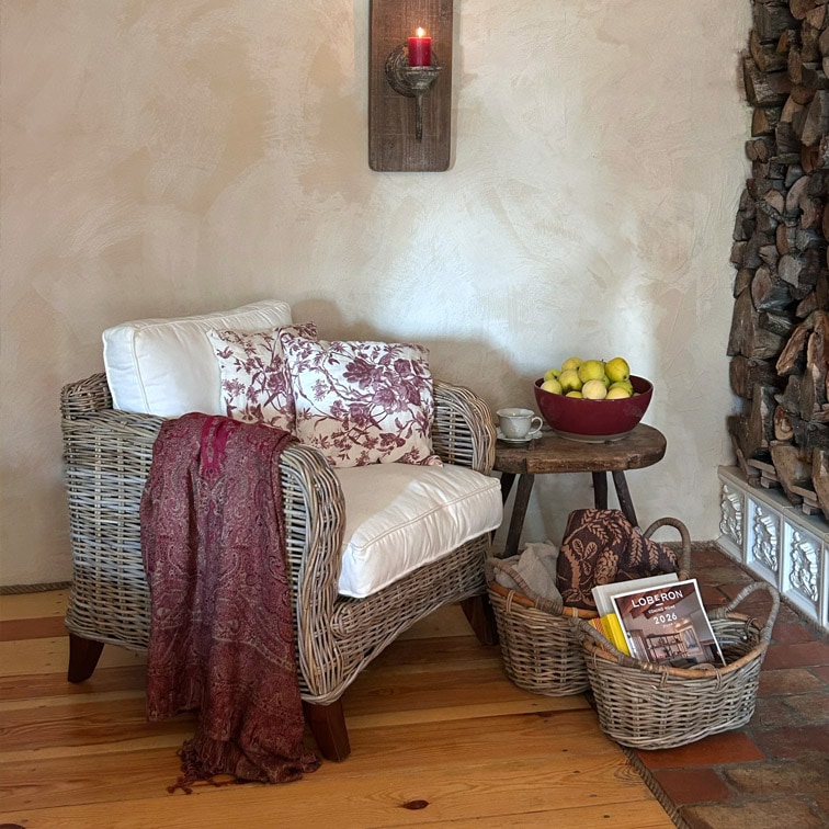 Fauteuil en osier avec coussin blanc et plaid bordeaux près d'une table en bois avec fruits et paniers