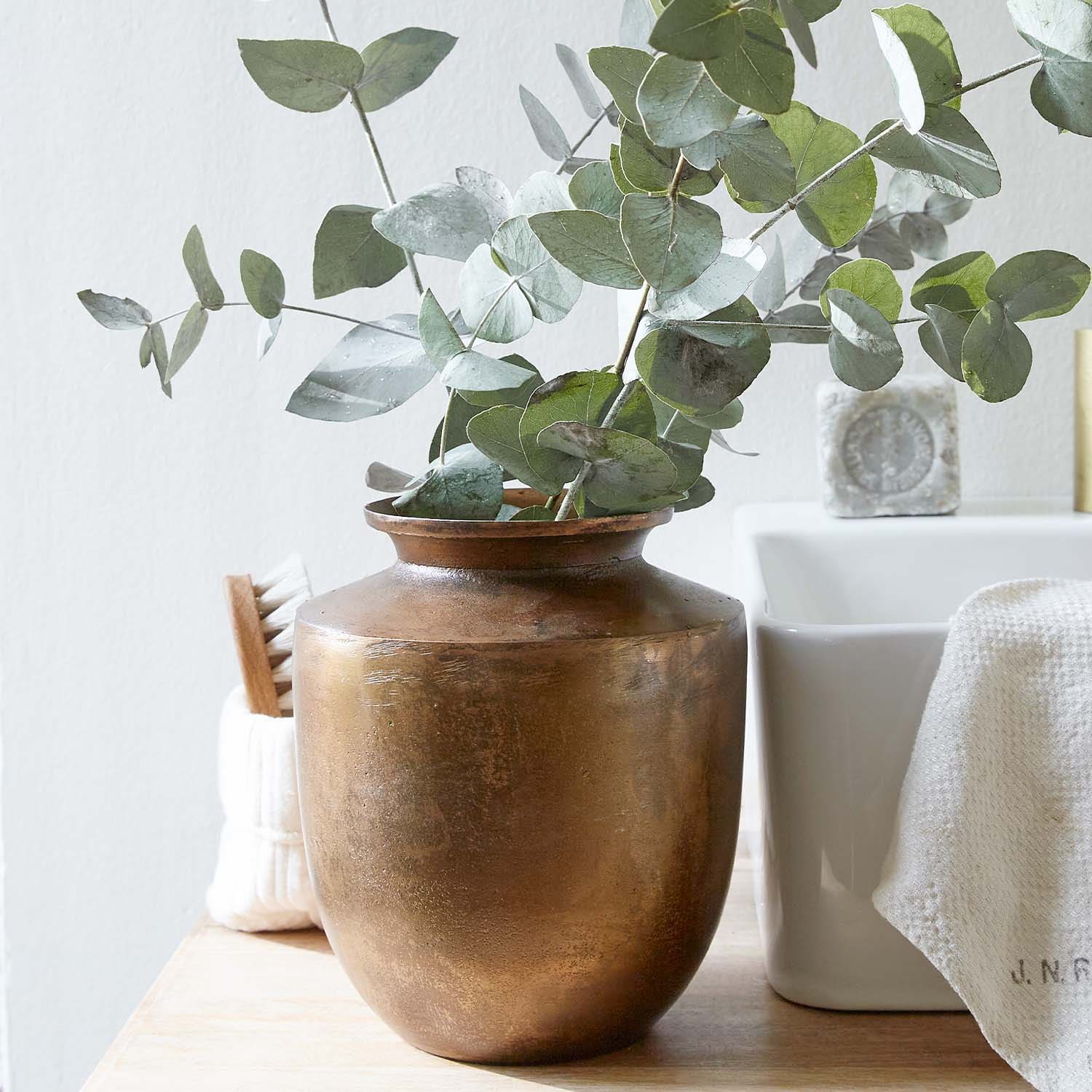 Vase en cuivre avec feuilles d'eucalyptus vertes sur une surface en bois dans un intérieur lumineux