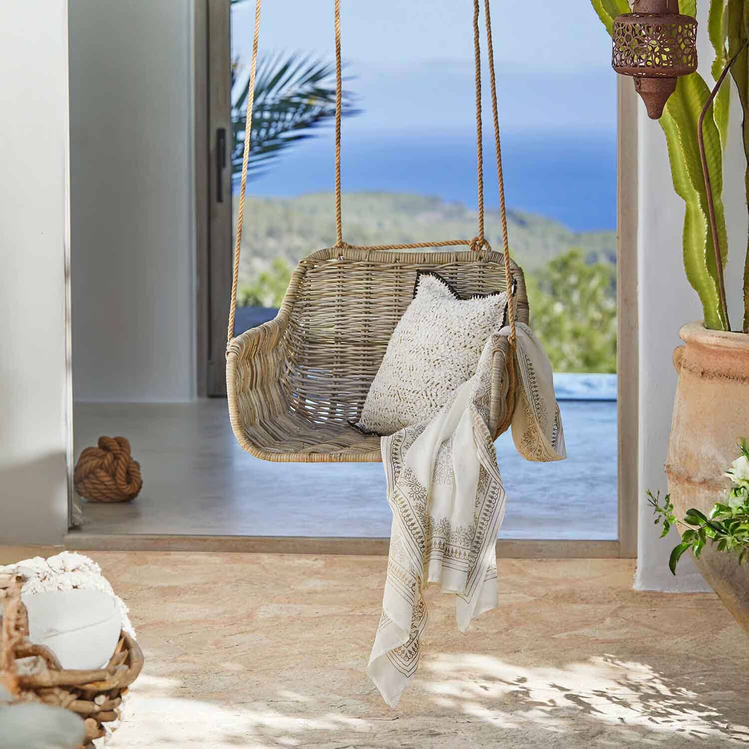Balançoire en rotin naturel avec coussin blanc et foulard décoratif dans un intérieur lumineux