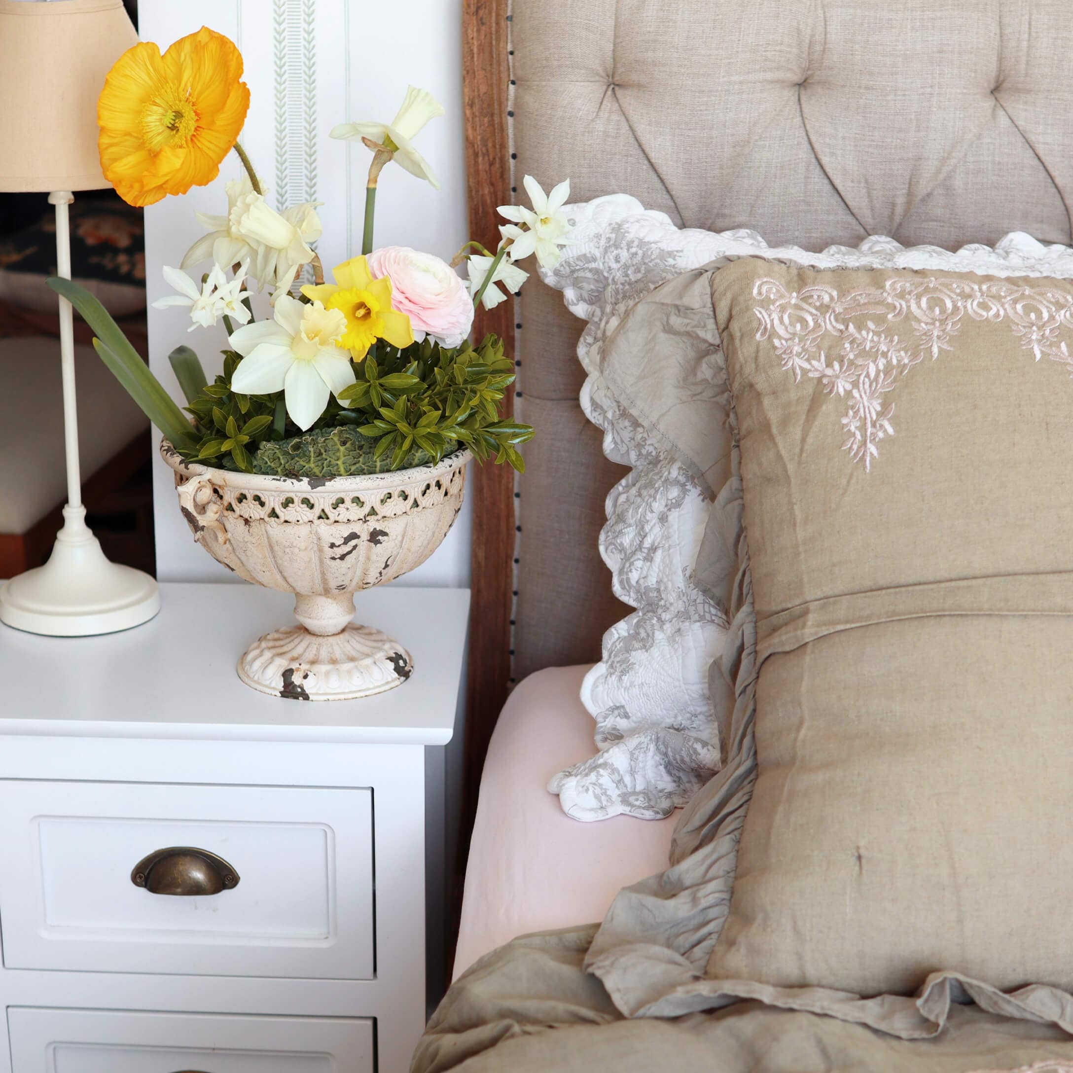 Vase décoratif blanc en céramique avec fleurs colorées sur table de chevet blanche près du lit