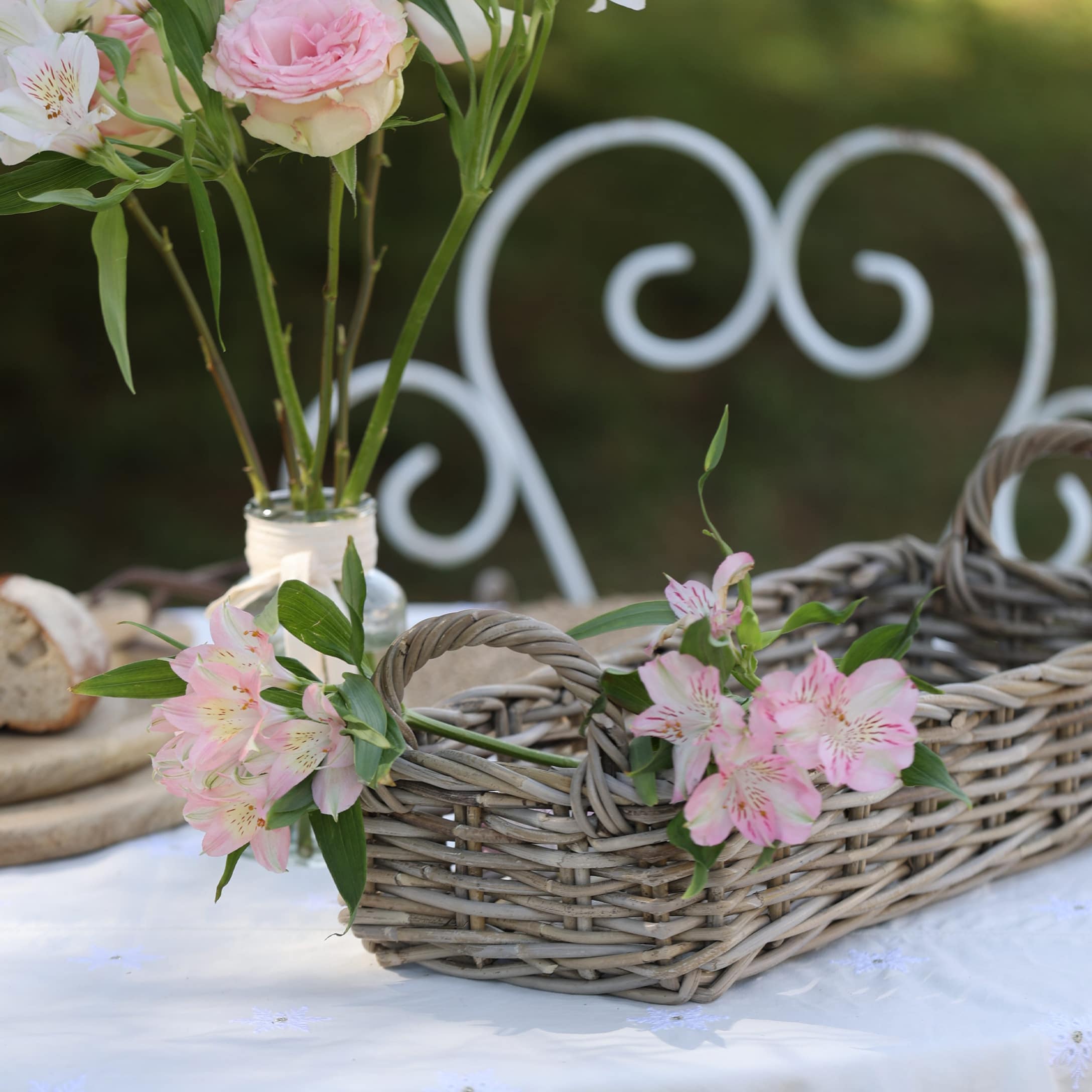 Panier en osier gris avec fleurs roses sur une nappe blanche dans un jardin extérieur