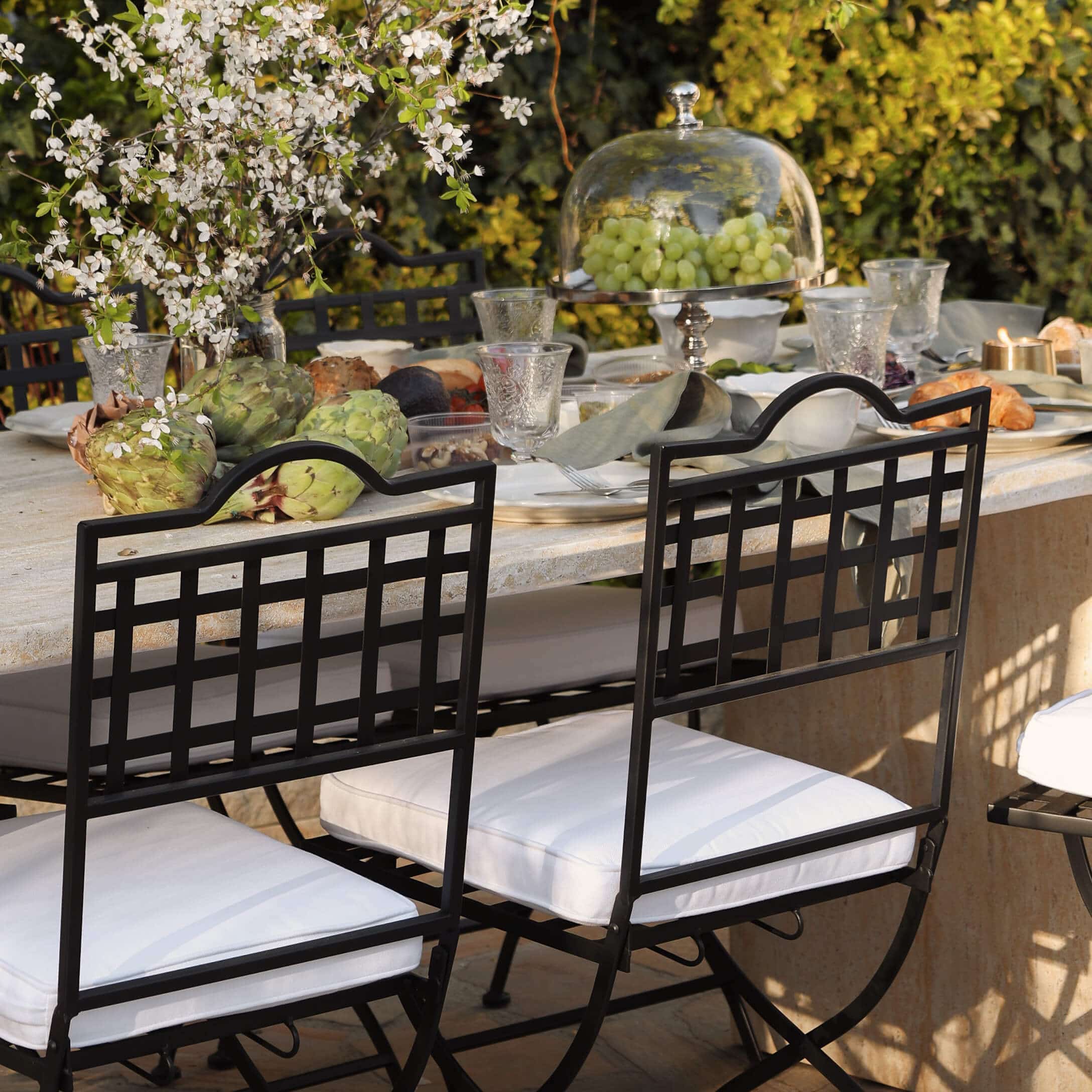 Chaises en métal noir avec coussins blancs autour d'une table en pierre décorée avec nourriture en extérieur