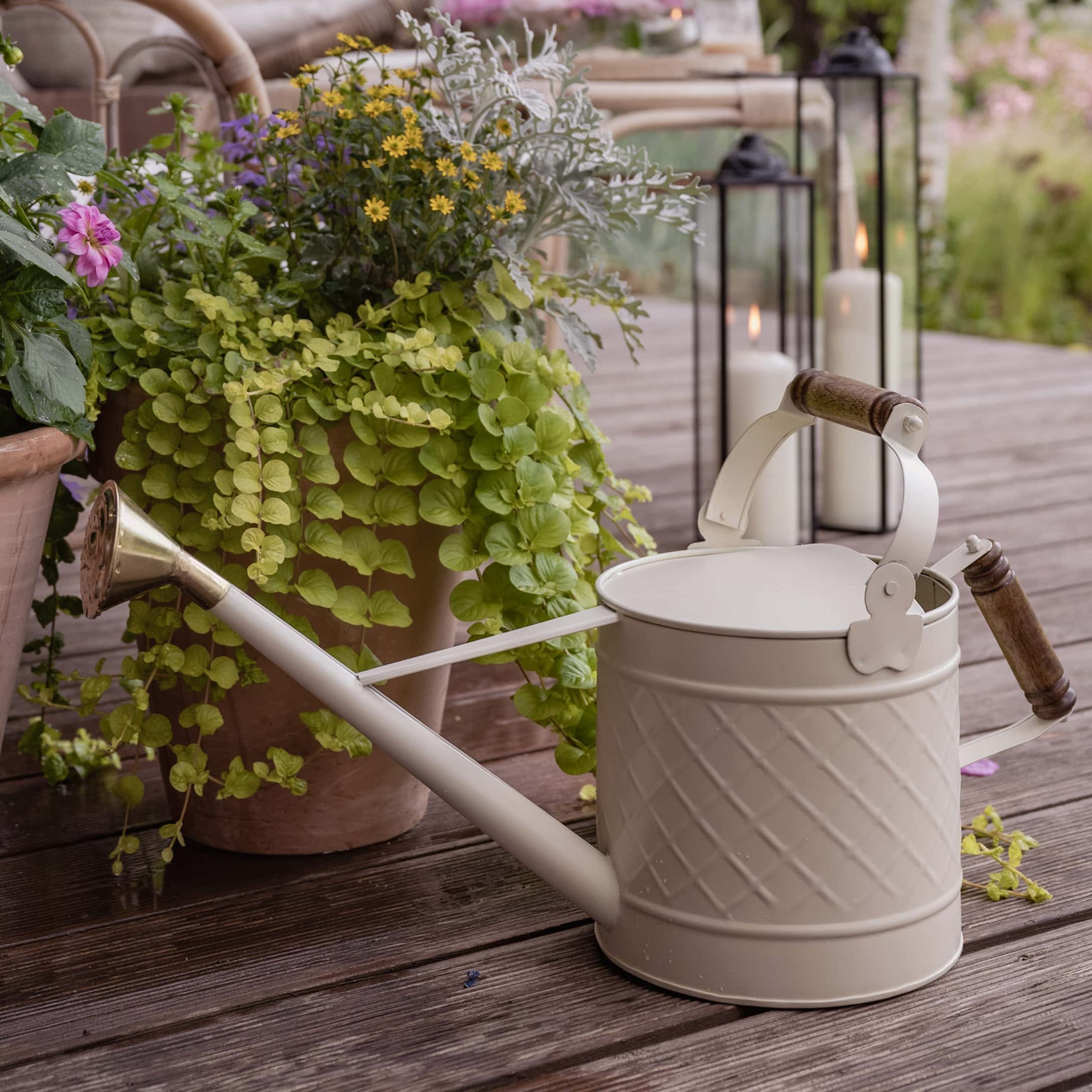 Arrosoir en métal crème avec poignées en bois sur terrasse en bois avec plantes et bougies
