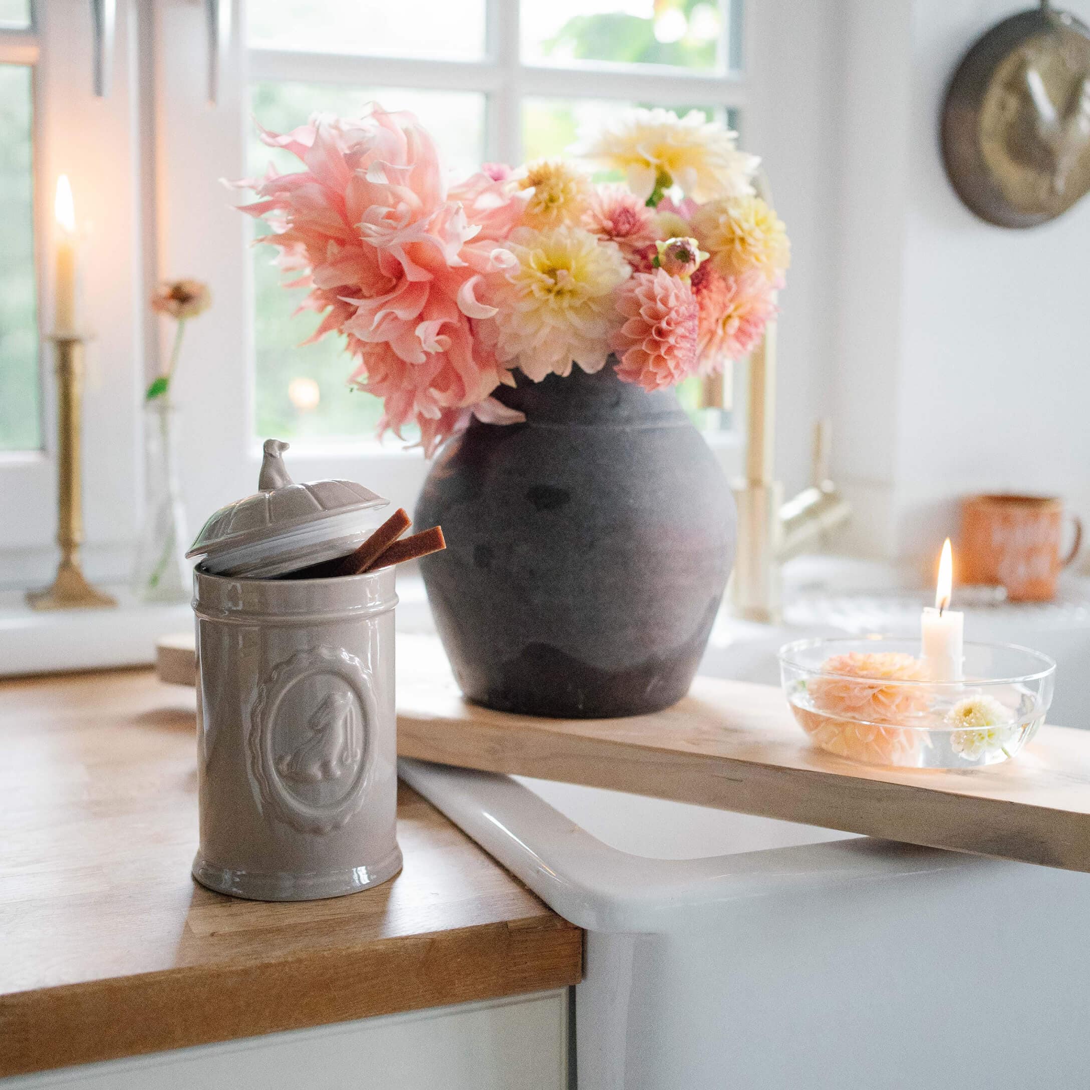 Boîte en céramique grise avec couvercle sur plan de travail en bois à côté d'un vase noir avec fleurs roses et jaunes