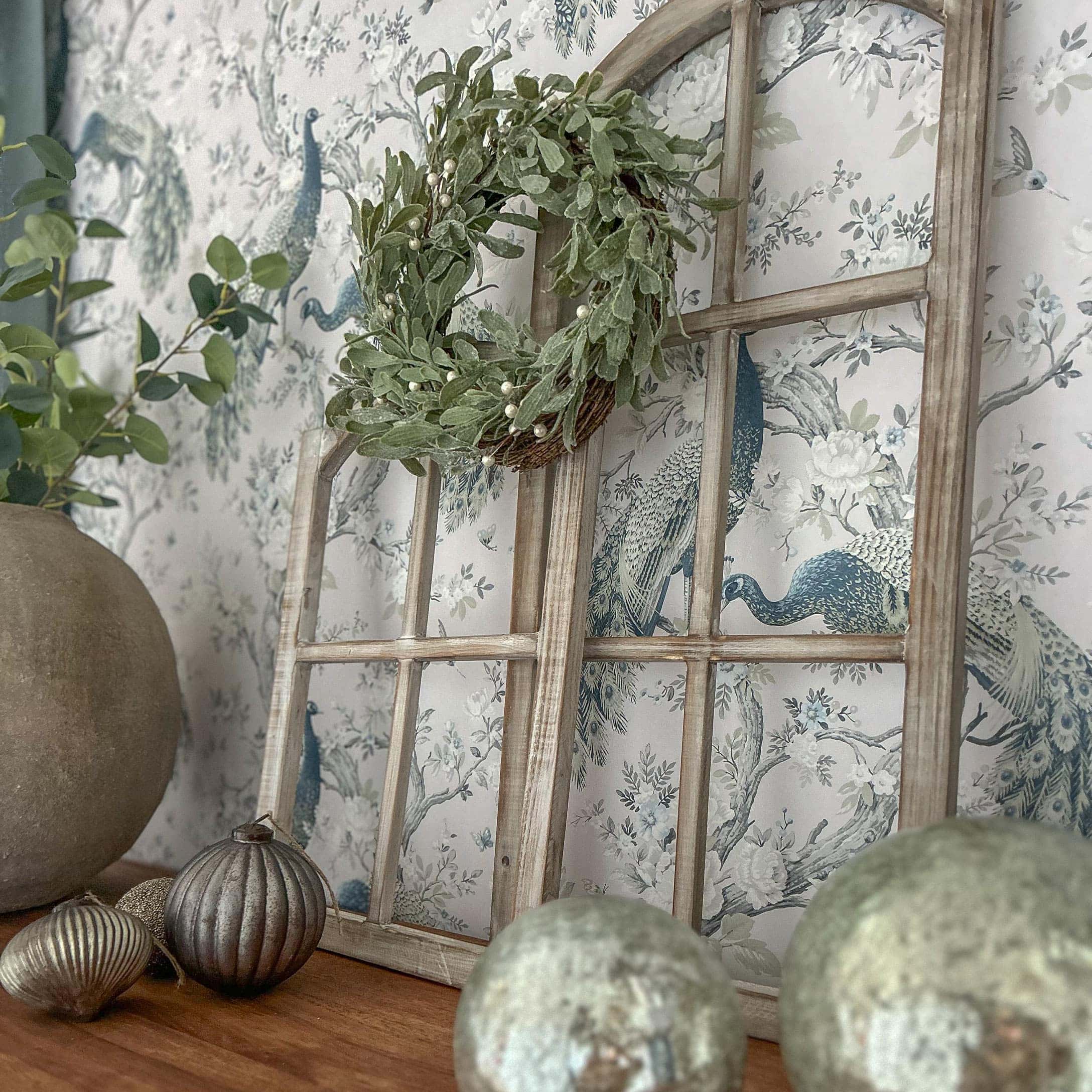 Cadre de fenêtre en bois décoratif avec couronne verte et ornements métalliques sur table en bois