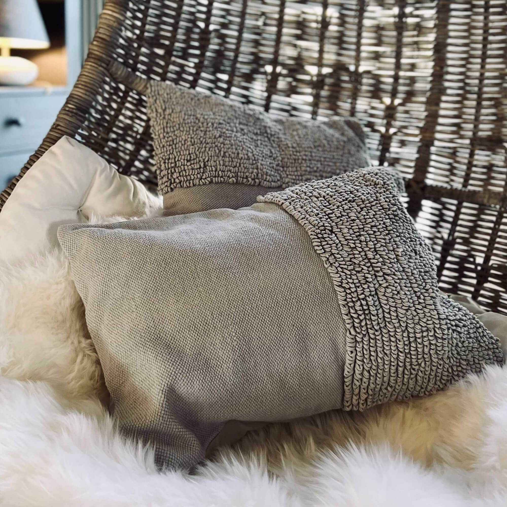 Coussin gris texturé sur fauteuil suspendu en osier avec couverture en fausse fourrure pour décoration intérieure