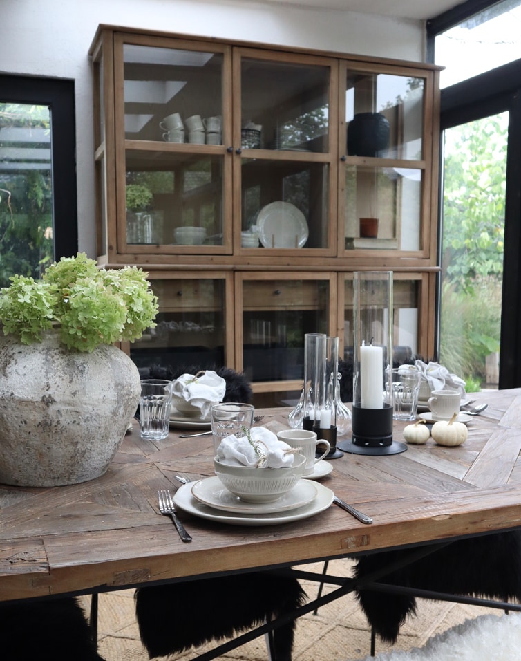 Table en bois rustique avec vaisselle et grand vase à fleurs vertes dans une orangerie lumineuse