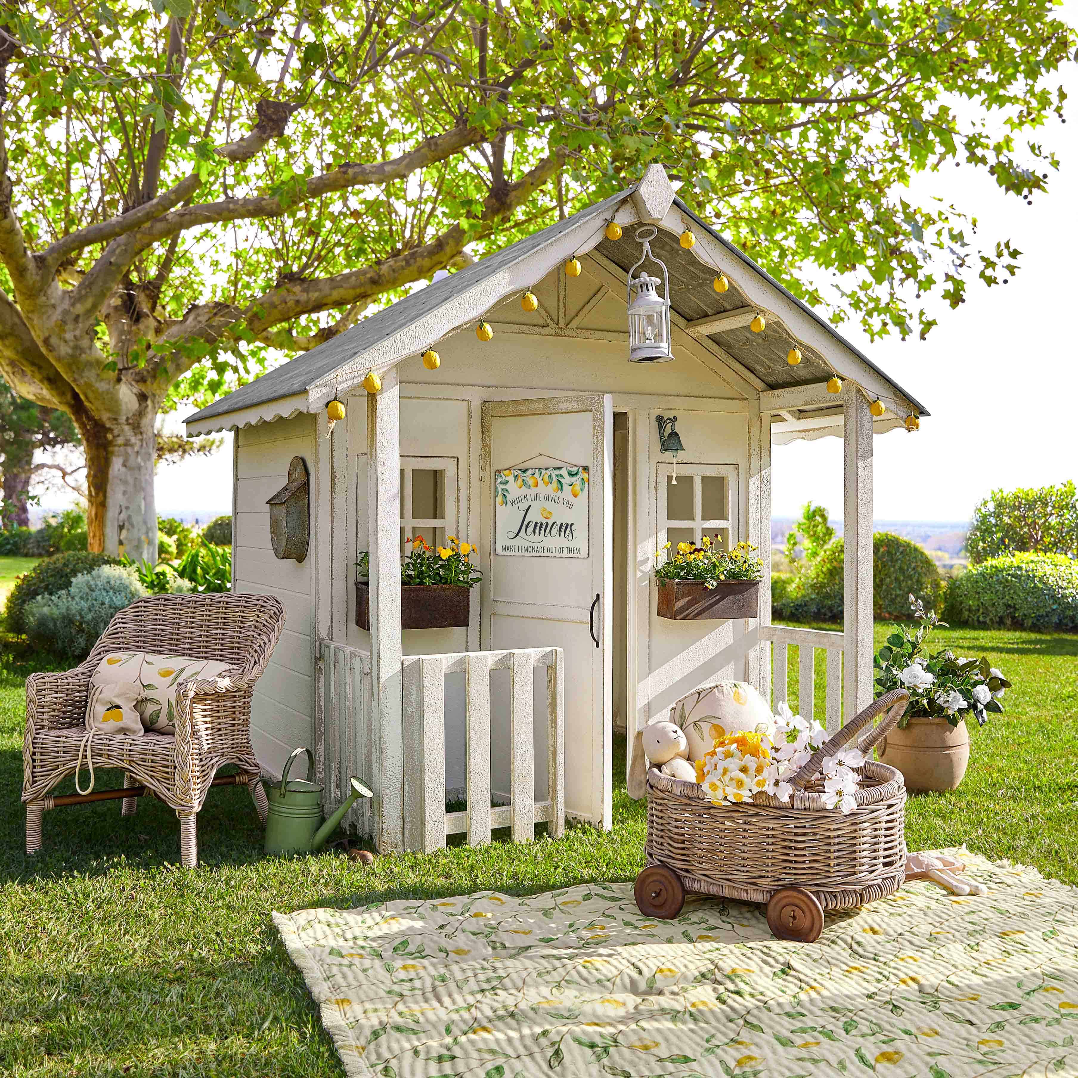 Maisonnette de jardin en bois blanc avec guirlande lumineuse et fleurs sur pelouse verte