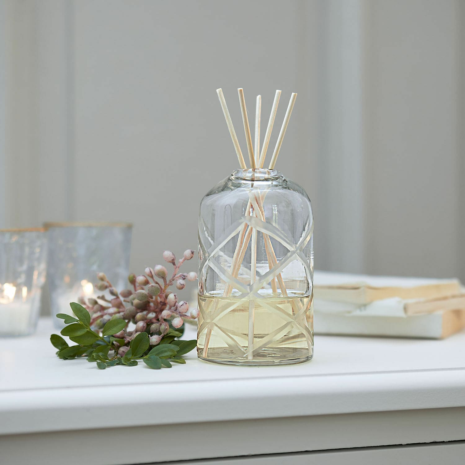 Parfum d’ambiance Azminah Diffuseur de parfum en verre avec bâtonnets naturels et huile jaune sur table blanche décorée