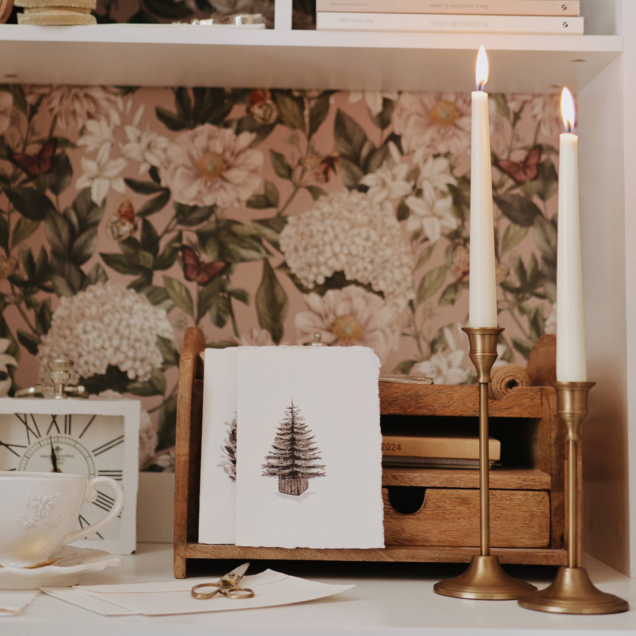 Organisateur en bois avec cartes de Noël et bougeoirs en laiton sur table blanche avec décor floral
