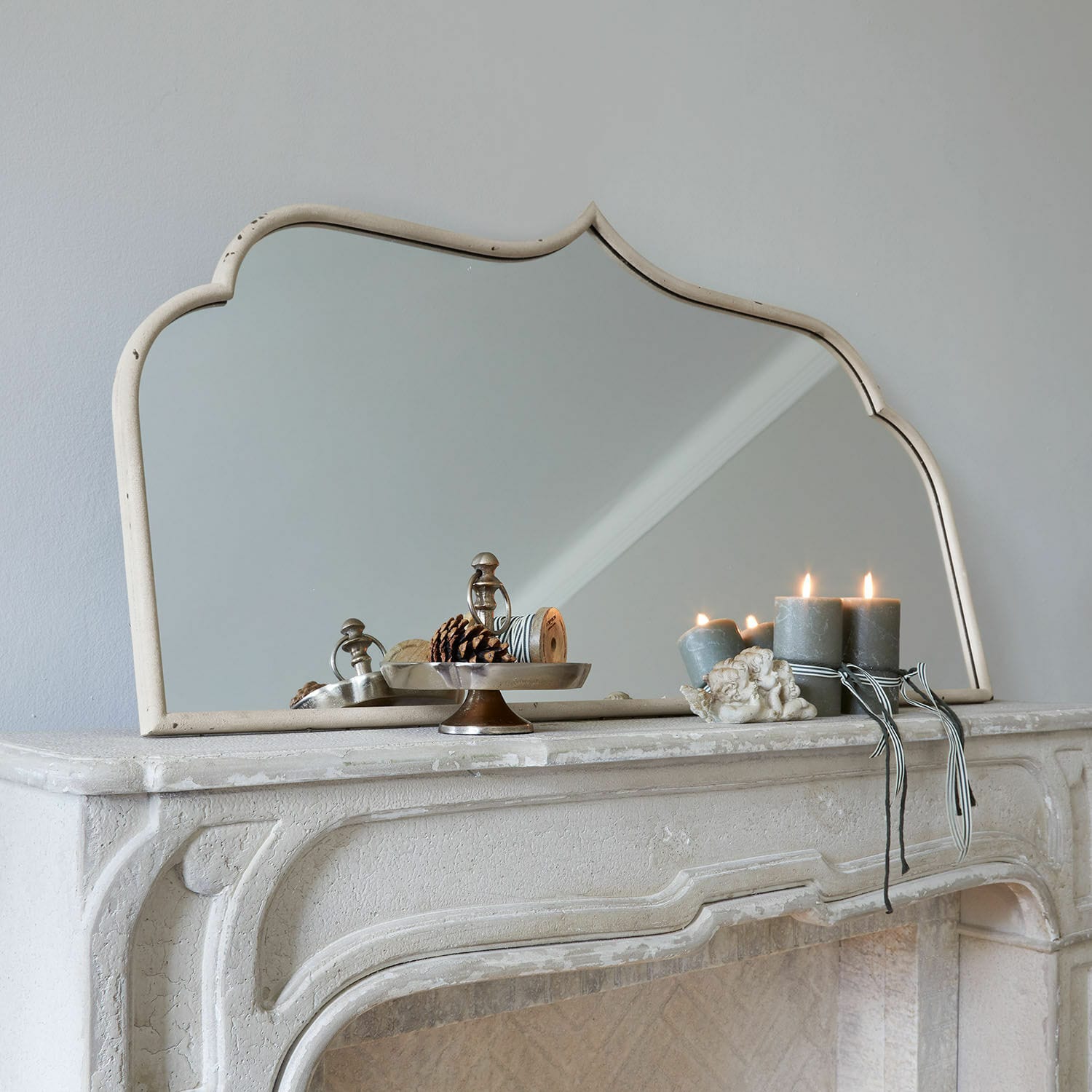Miroir Selamira Miroir décoratif à cadre beige posé sur une cheminée en pierre avec bougies et pommes de pin