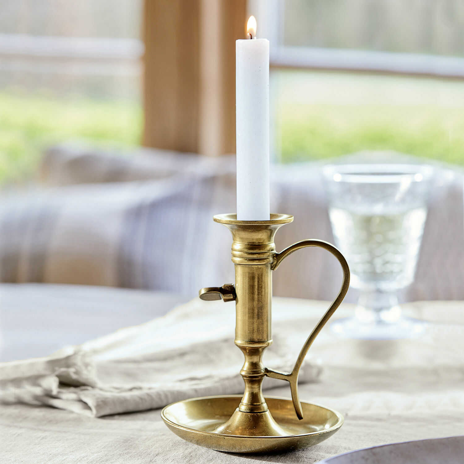Bougeoir Carmel Chandelier en laiton avec poignée et bougie blanche sur nappe en lin, décoration de table