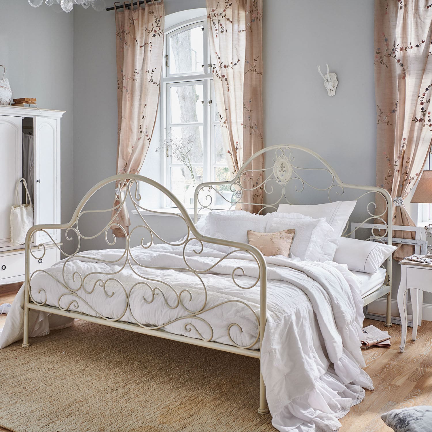 Lit Moissac Lit en métal crème style vintage avec literie blanche et coussin décoratif dans une chambre lumineuse