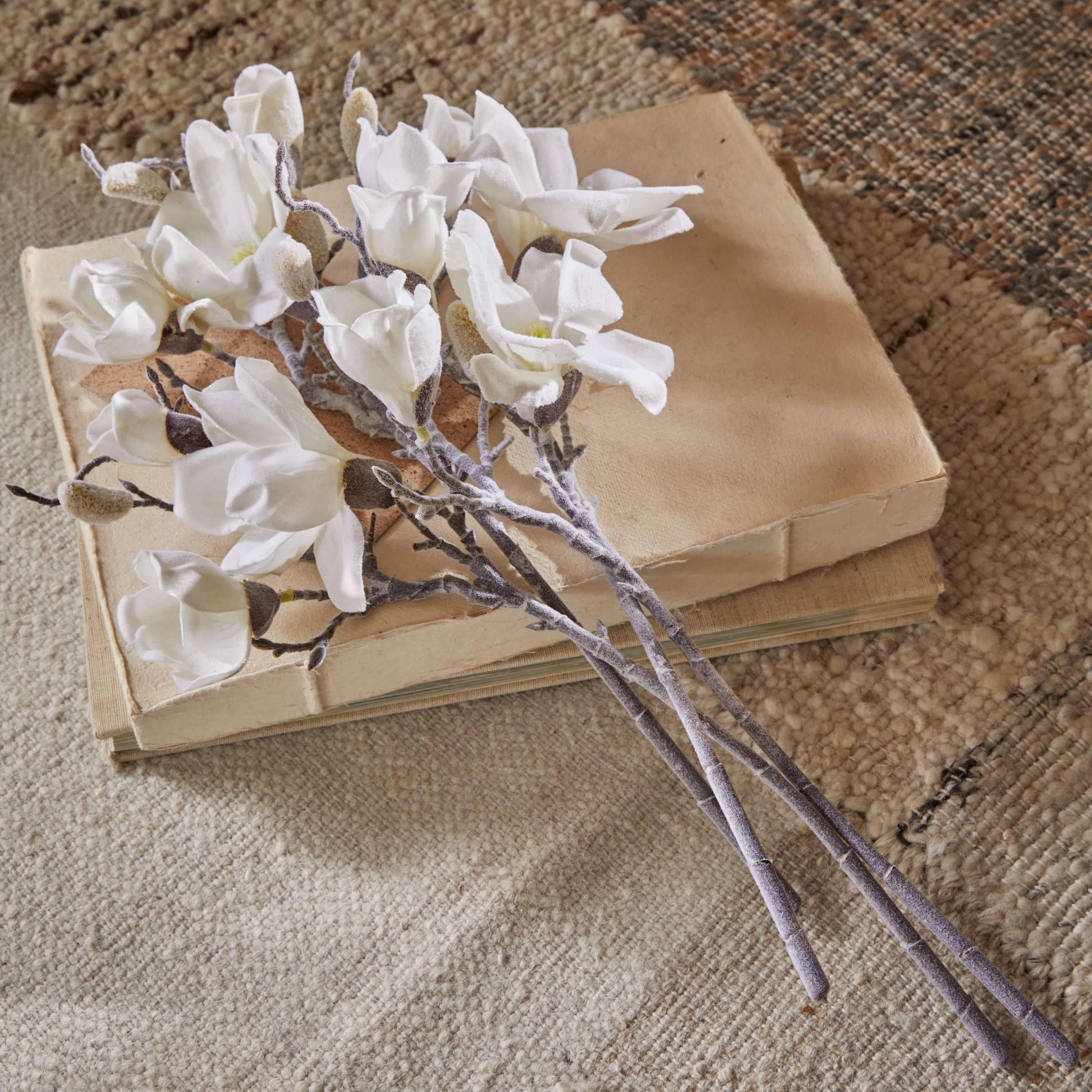 Bouquet de fleurs de magnolia blanches en tissu posé sur des livres anciens beiges sur un tapis