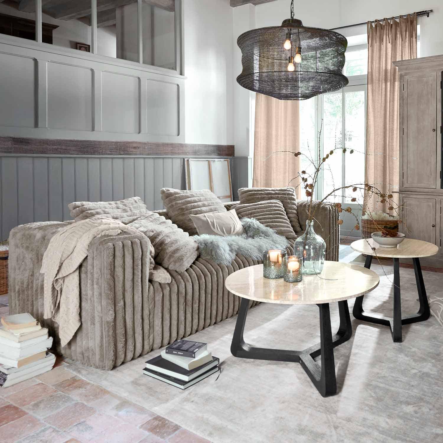 Canapé beige en tissu doux dans un salon moderne avec deux tables basses rondes en bois et métal
