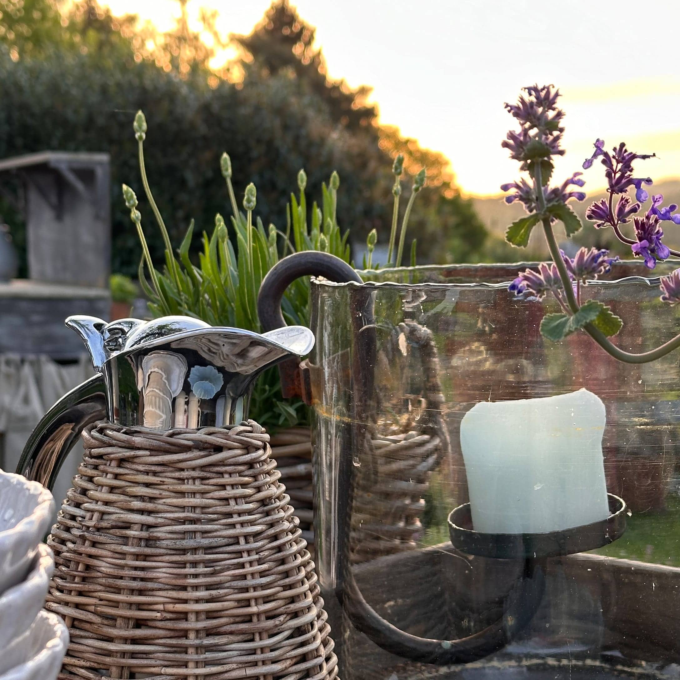 Pichet en métal avec tressage en osier et bougeoir en verre dans un jardin d'été