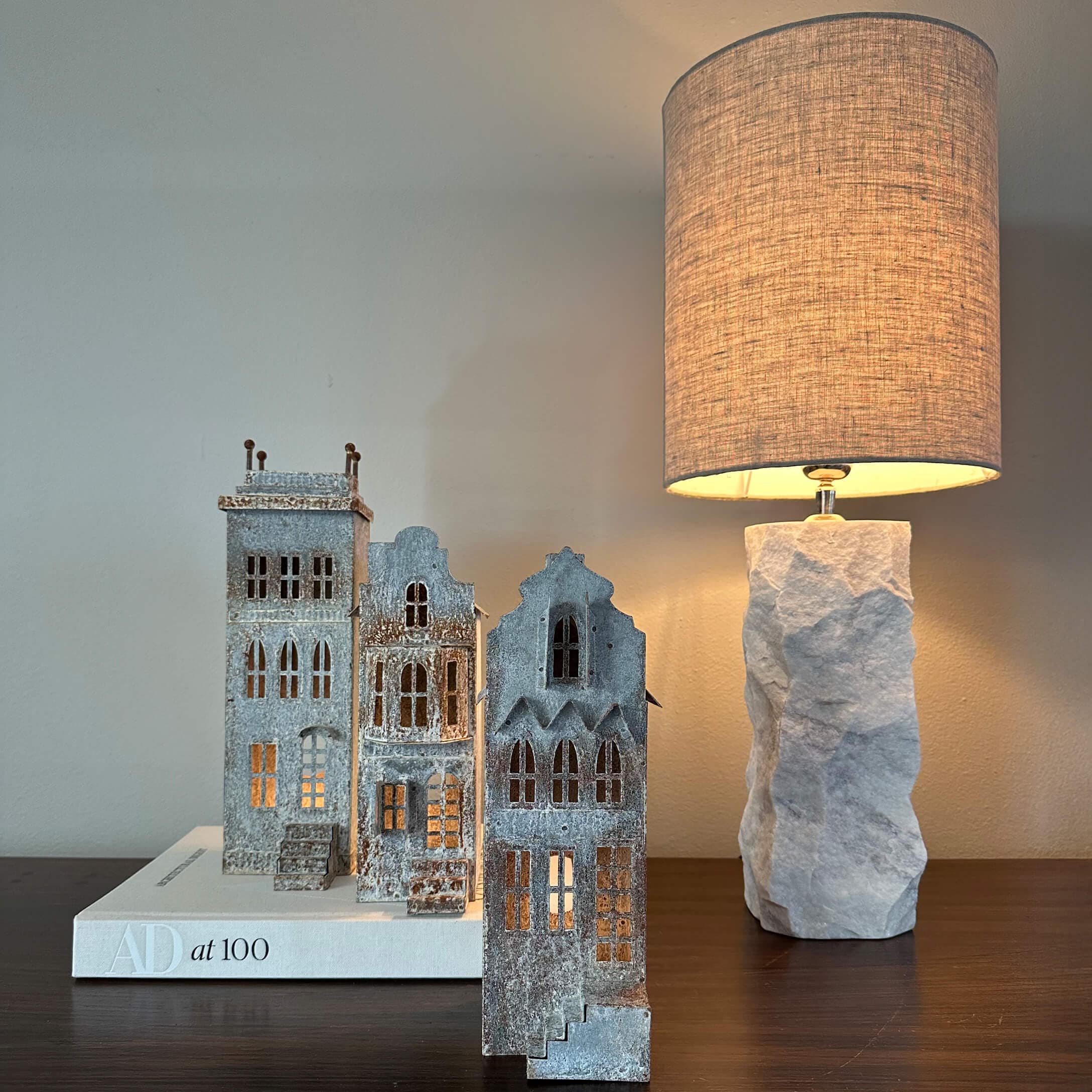 Maisons décoratives en métal gris posées sur un livre blanc à côté d'une lampe avec base en pierre
