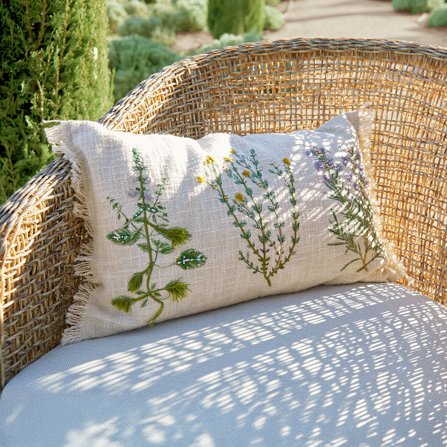 Coussin en lin beige avec broderie végétale sur fauteuil en osier, décoration extérieure